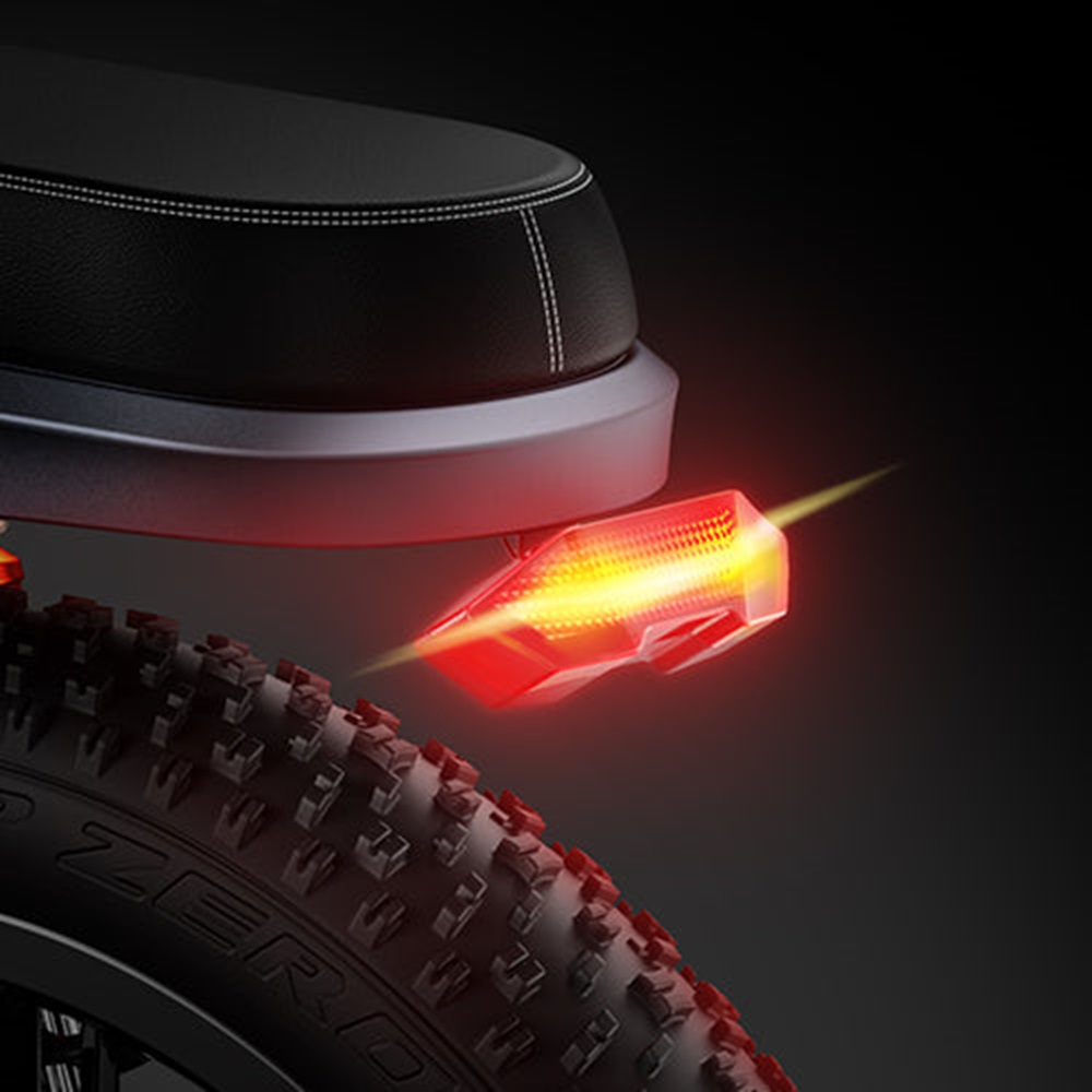 Una luz roja de bicicleta está iluminada. Está montada en la parte trasera de una bicicleta, sobre el neumático, sobre un fondo oscuro.