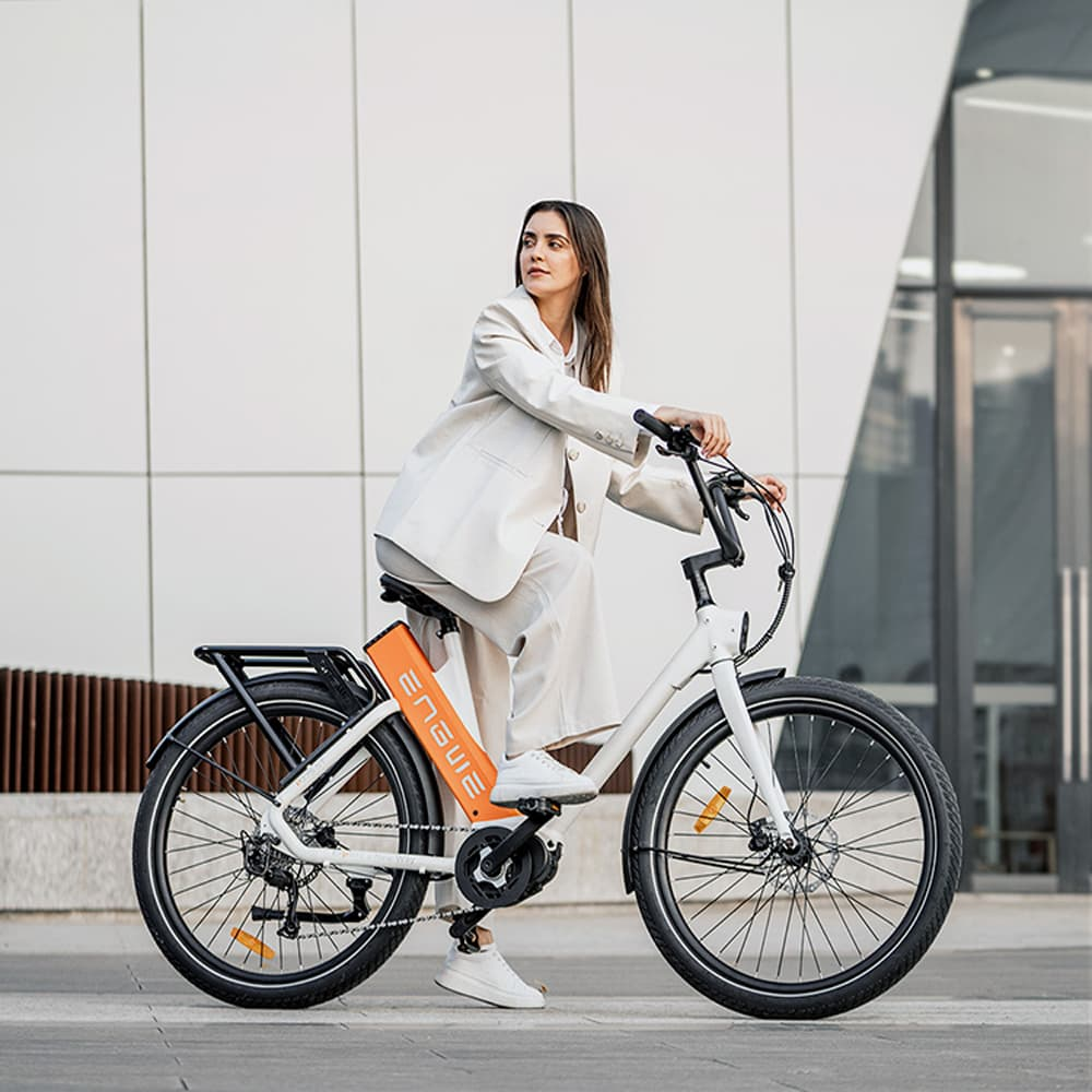 Una mujer monta en bicicleta eléctrica en una calle, con traje blanco y zapatillas.