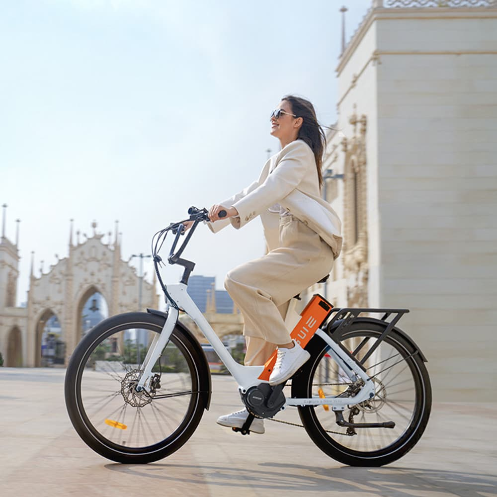Mujer en e-bike blanca, en día soleado, con edificio al fondo.