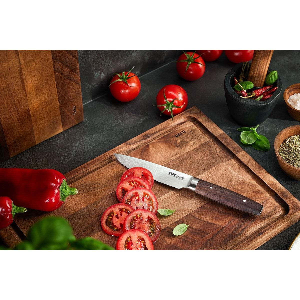 Tomaten und geschnittene Tomaten auf einem Holzschneidebrett mit Messer und anderen Zutaten.