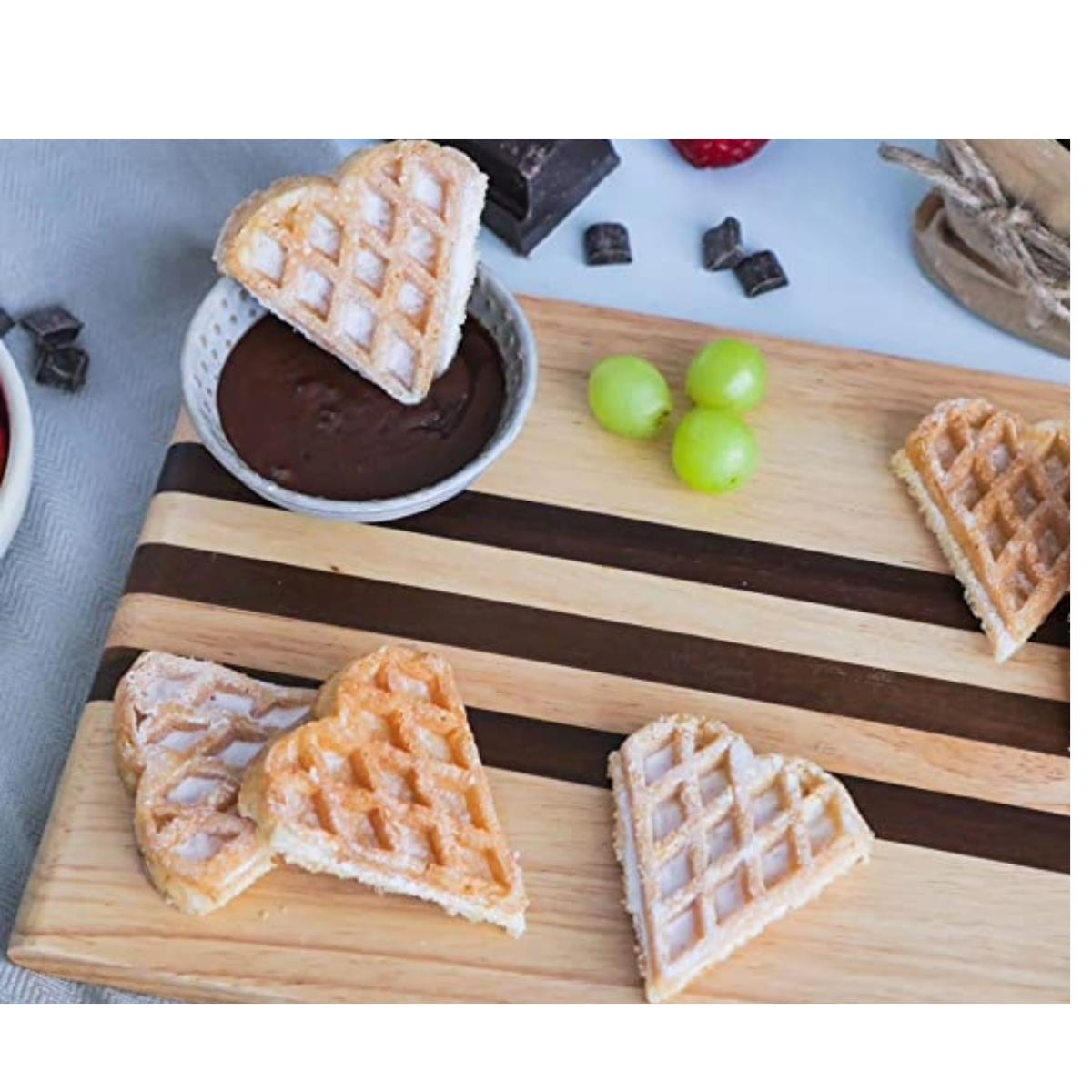 Herzförmige Waffeln mit Schokoladendipp und Trauben auf einem Holzbrett. Einige Waffeln sind aufgeschnitten.