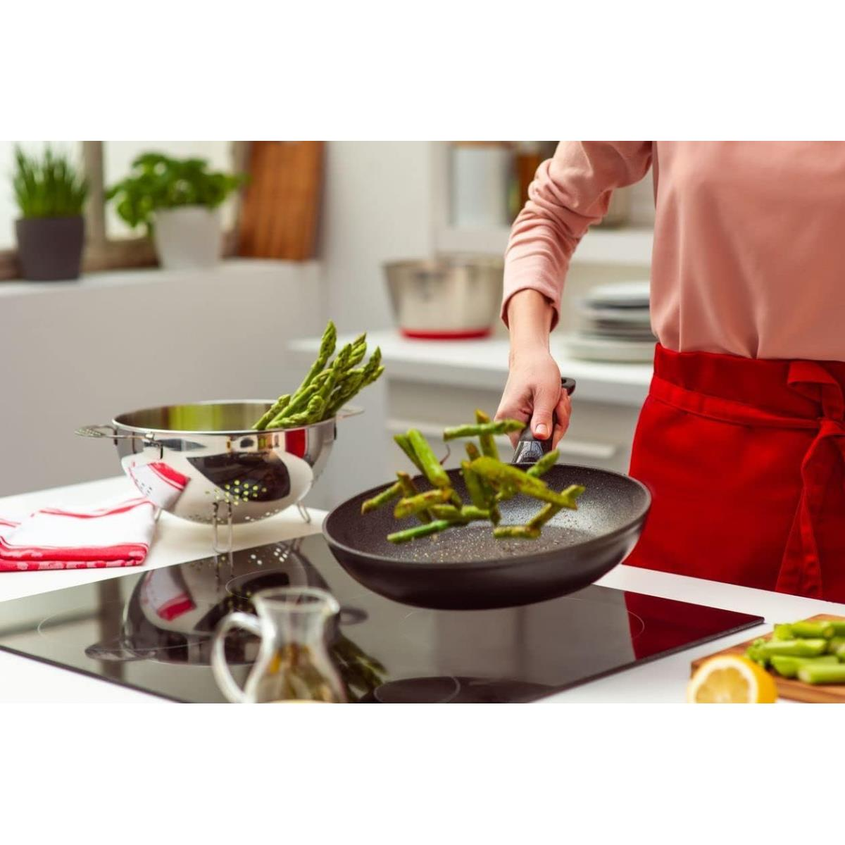 Persona che getta asparagi in una padella su un piano cottura in una cucina.