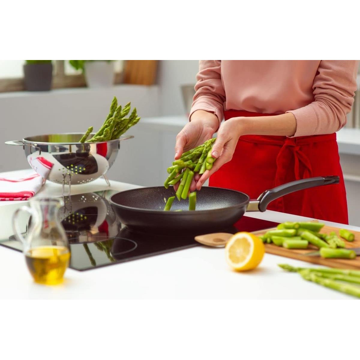 Una persona aggiunge asparagi a una padella su un fornello. Altri ingredienti sono nelle vicinanze.
