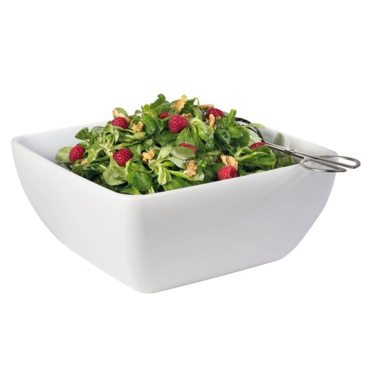 Eine quadratische weiße Schüssel gefüllt mit Salat, belegt mit Himbeeren und Nüssen, mit Servierzangen.
