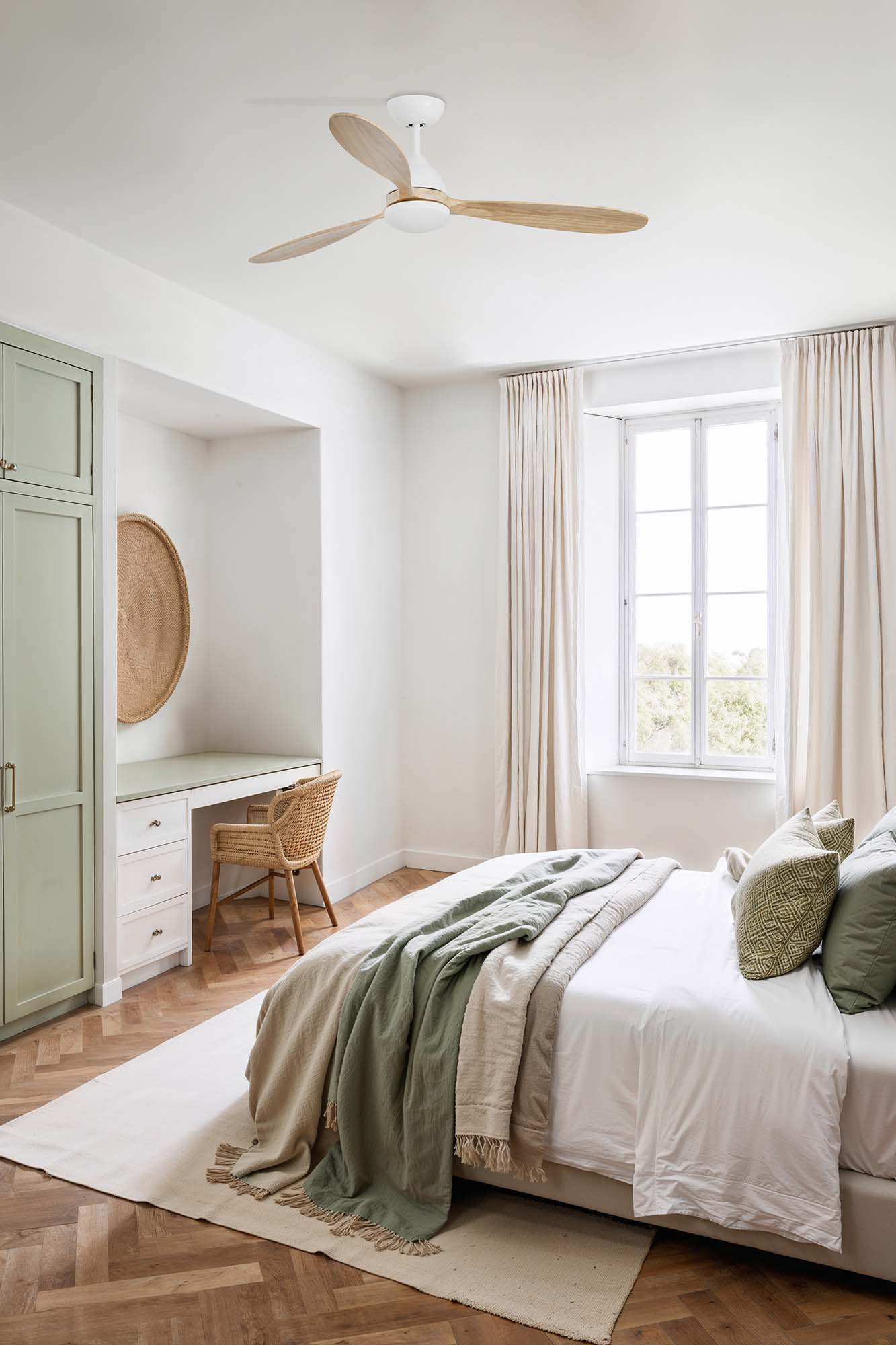 Camera da letto con letto, ventilatore a soffitto e finestra. Accenti verdi, pavimento in legno chiaro e pareti bianche.
