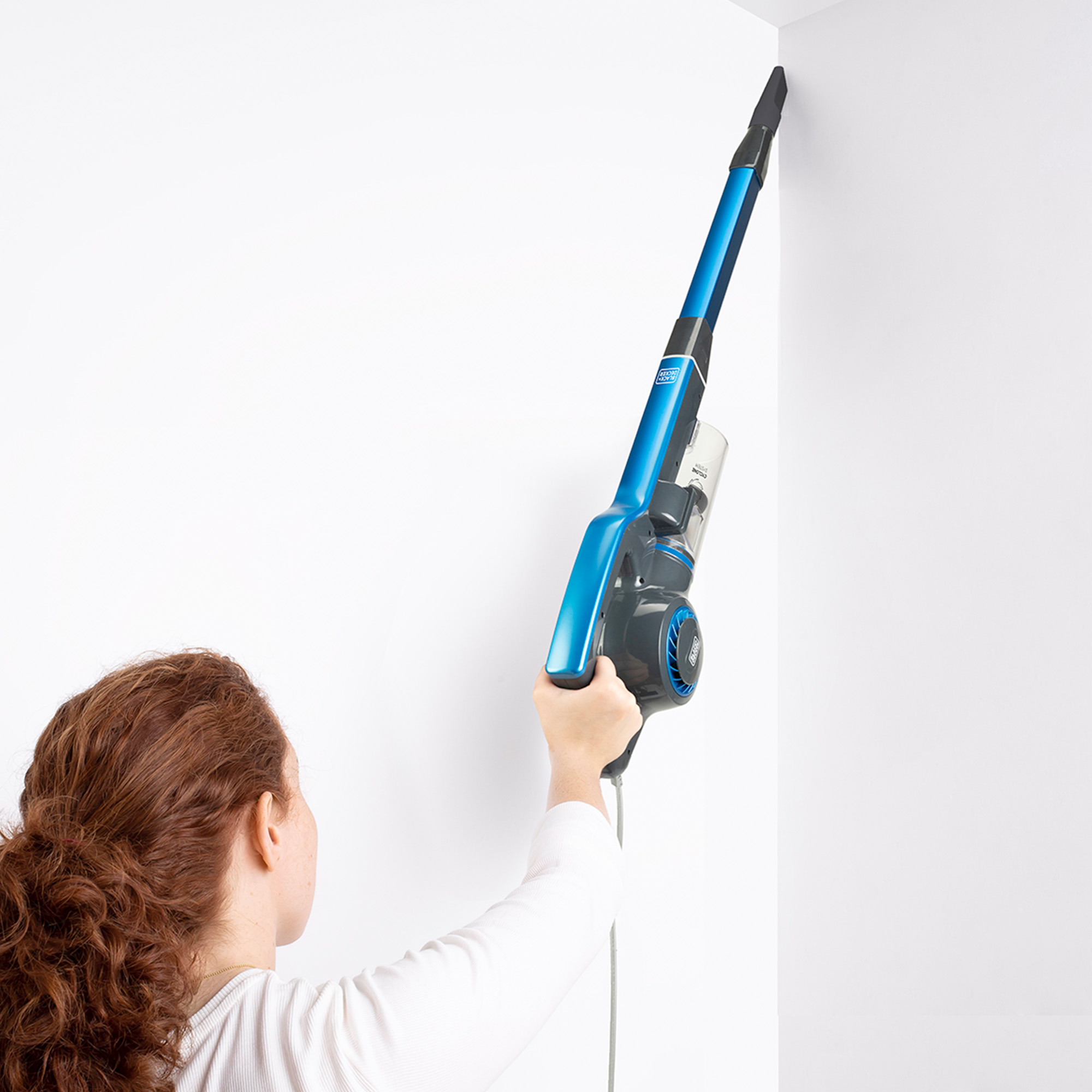 Kobieta używająca niebiesko-czarnego odkurzacza w białym rogu pokoju.