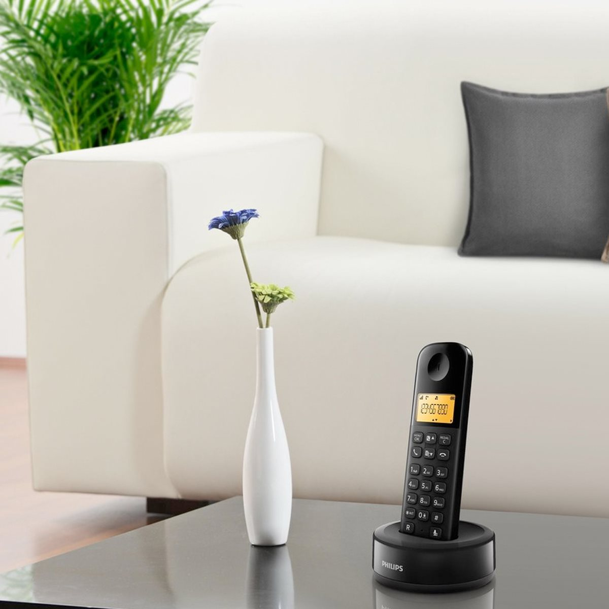 Un téléphone sans fil sur une base de chargement, un vase avec des fleurs et un canapé sur une table.