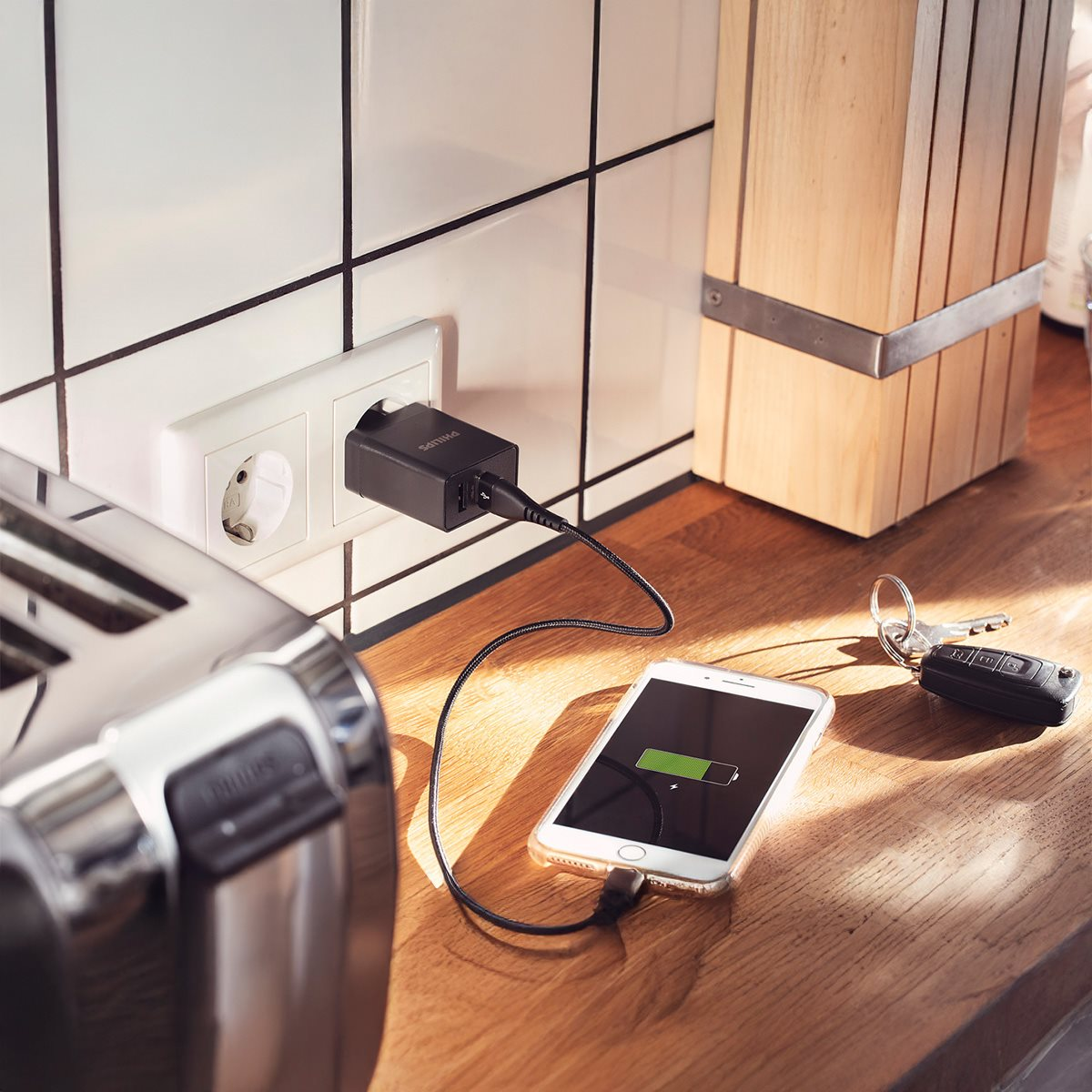 Telefoon wordt opgeladen met een zwarte oplader in een stopcontact. Houten oppervlak.