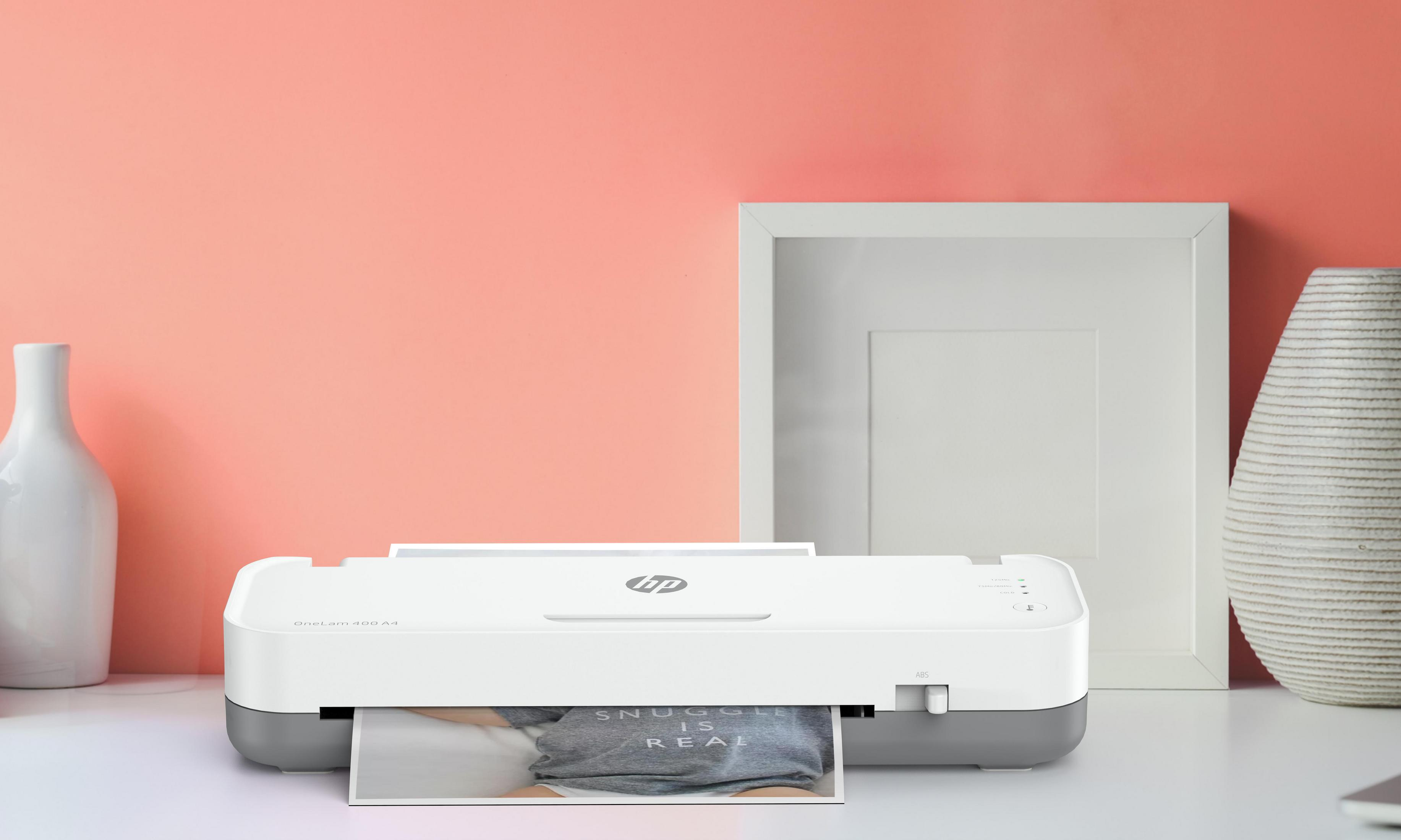 Drukarka HP na biurku z ramką na zdjęcia i wazonem. Drukarka drukuje zdjęcie.