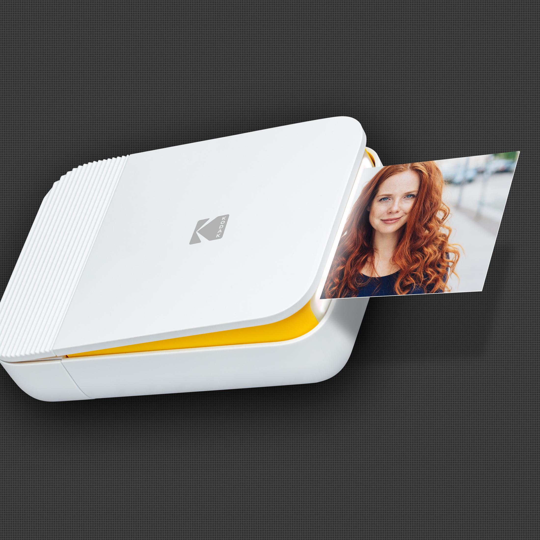 Ein weißer und gelber Kodak Fotodrucker mit einem gedruckten Foto, das eine Frau mit roten Haaren zeigt.
