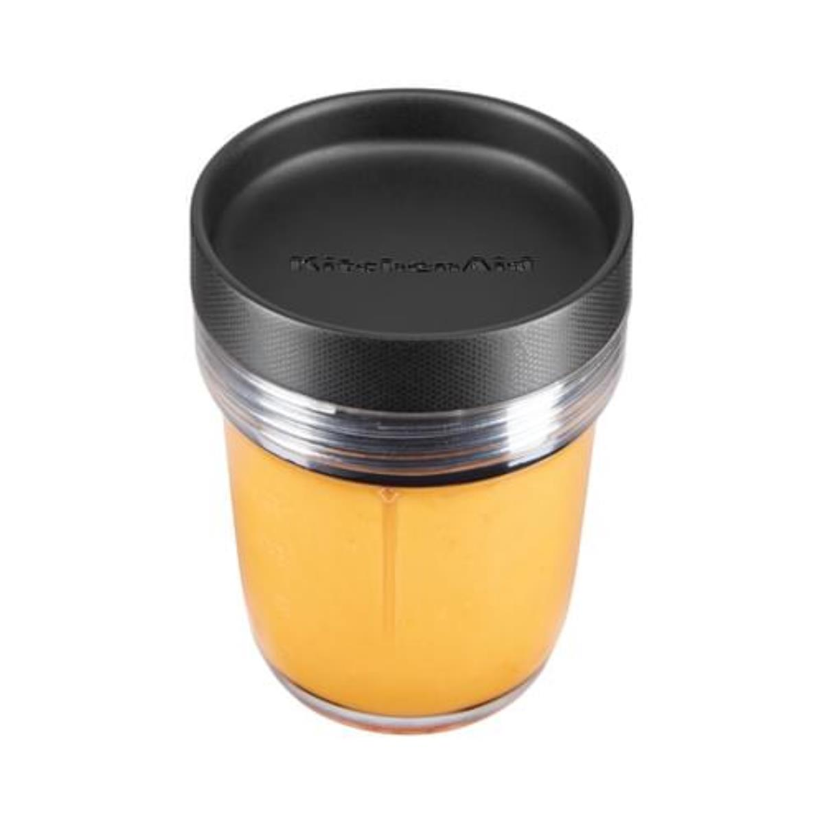 Ein klarer KitchenAid-Blenderbecher mit schwarzem Deckel, gefüllt mit orangener Flüssigkeit.