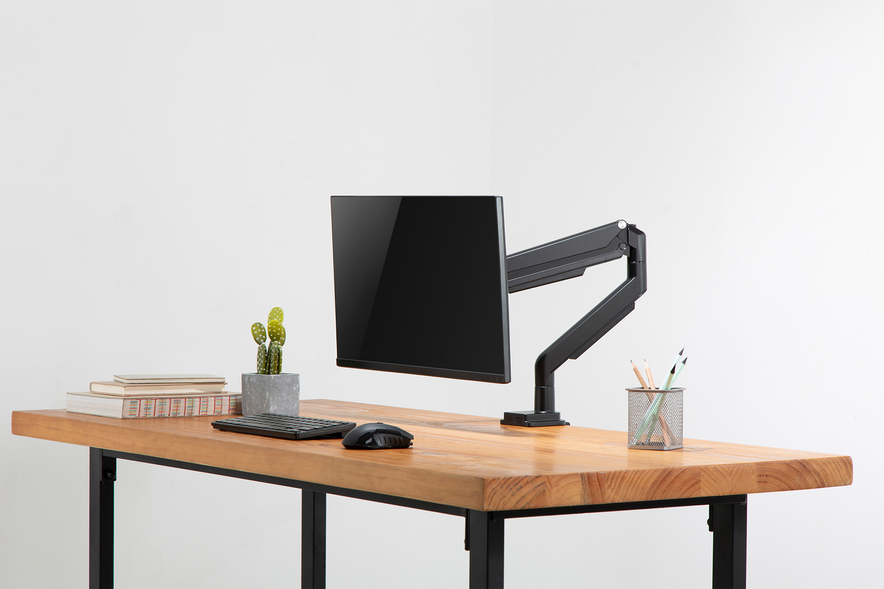 Monitor na biurku. Klawiatura, mysz, kaktus i ołówki. Drewniane biurko, czarna rama. Białe tło.