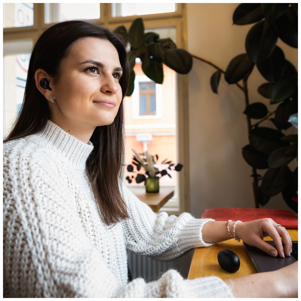 Frau mit Kopfhörern beim Zuhören. Sie lächelt, während sie an einem Tisch mit Laptop sitzt.
