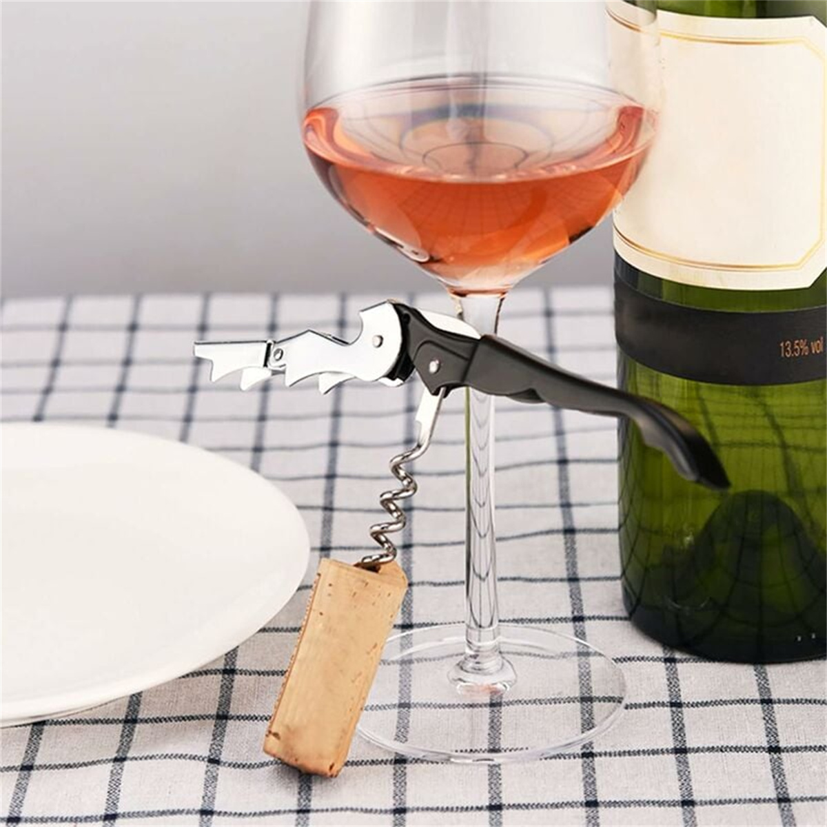 Ein Korkenzieher, der einen Korken aus einem Weinglas entfernt. Das Glas enthält Roséwein, auf kariertem Tuch.