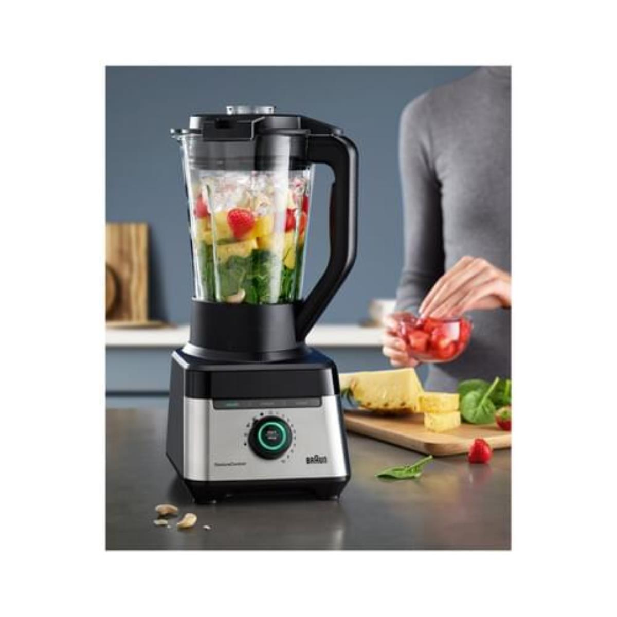 Ein Mixer mit Früchten und einer Person, die Zutaten zubereitet. Es sieht nach Kochen aus.