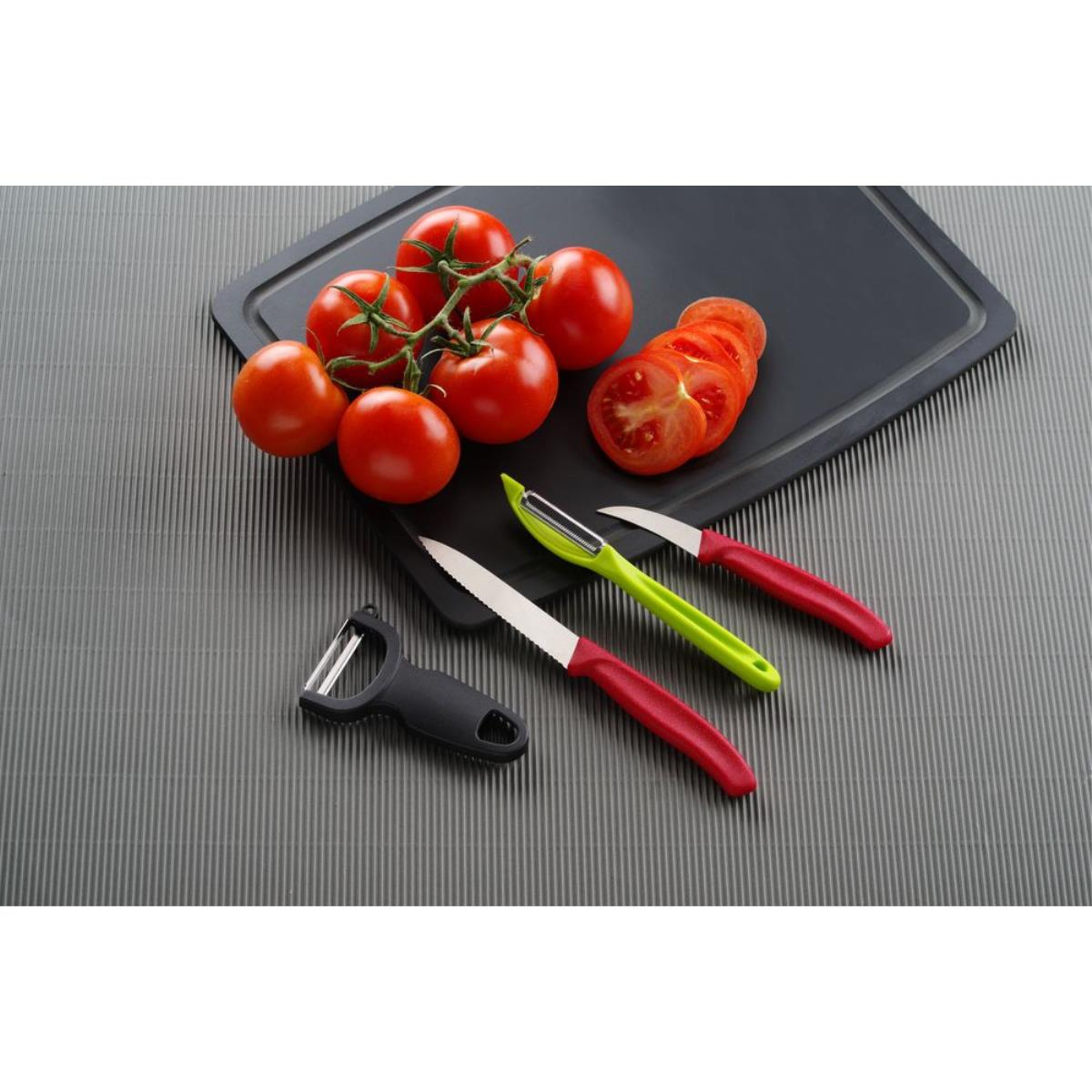 Tomaten, ein Tomatenzweig und drei Küchenmesser auf einem schwarzen Schneidebrett.