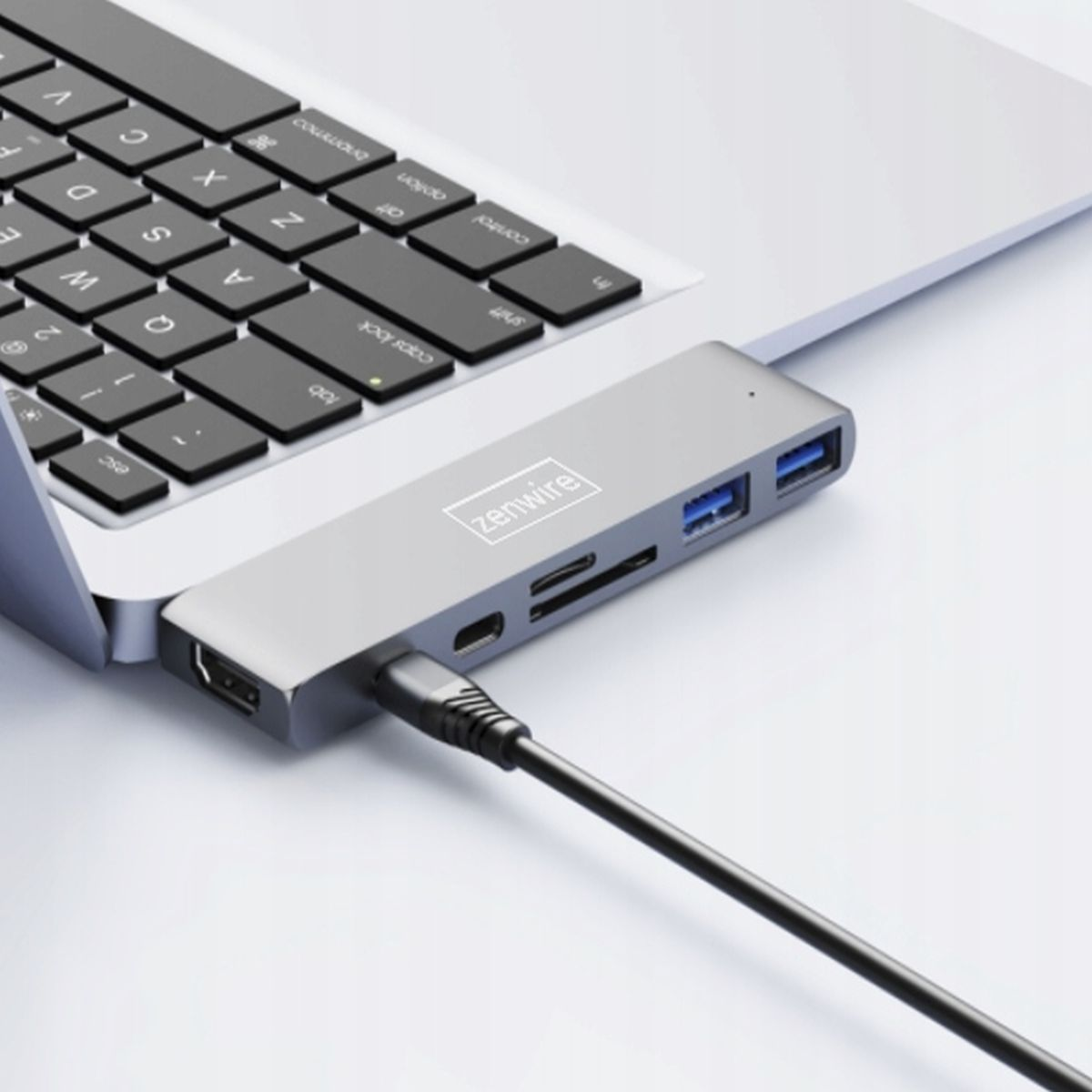 Laptop podłączony do srebrnego huba z wieloma portami, czarny kabel.