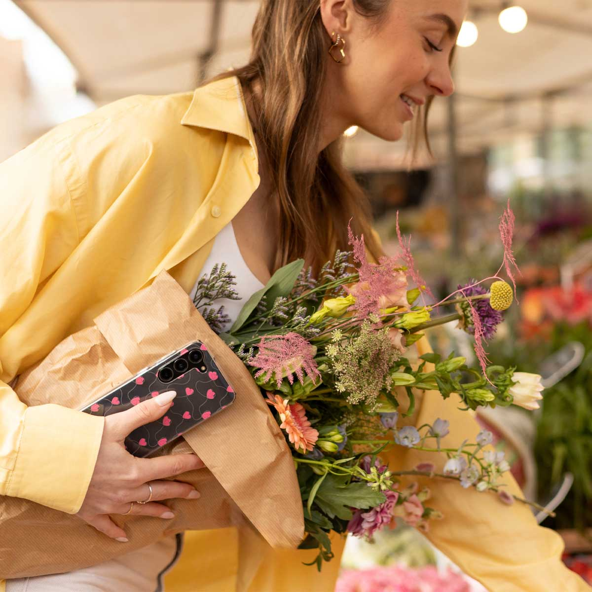 Frau mit Blumen und schwarzer Handyhülle. Sie trägt ein gelbes Hemd.