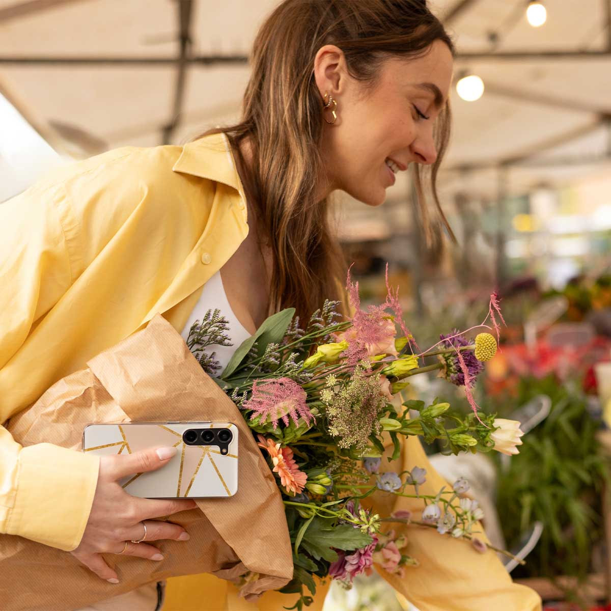 Frau mit Blumen, hält ein Telefon. Das Telefon hat ein weißes und goldenes Design.
