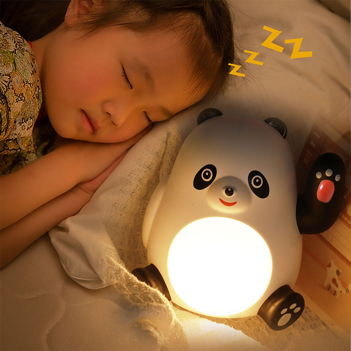 Ein schlafendes Mädchen neben einem Panda-Nachtlicht. Das Licht ist an. Der Hintergrund ist ein Bett und eine Decke.
