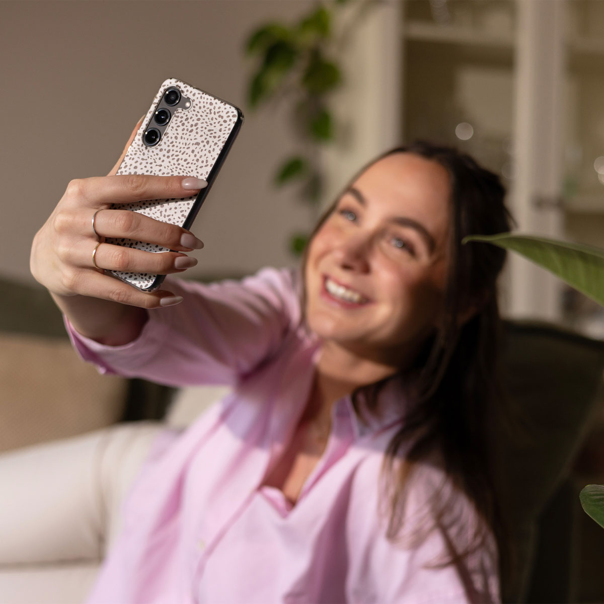 Eine Frau macht ein Selfie mit einem Telefon in ihrer rechten Hand. Sie lächelt. Das Telefon hat eine weiße, gemusterte Rückseite.