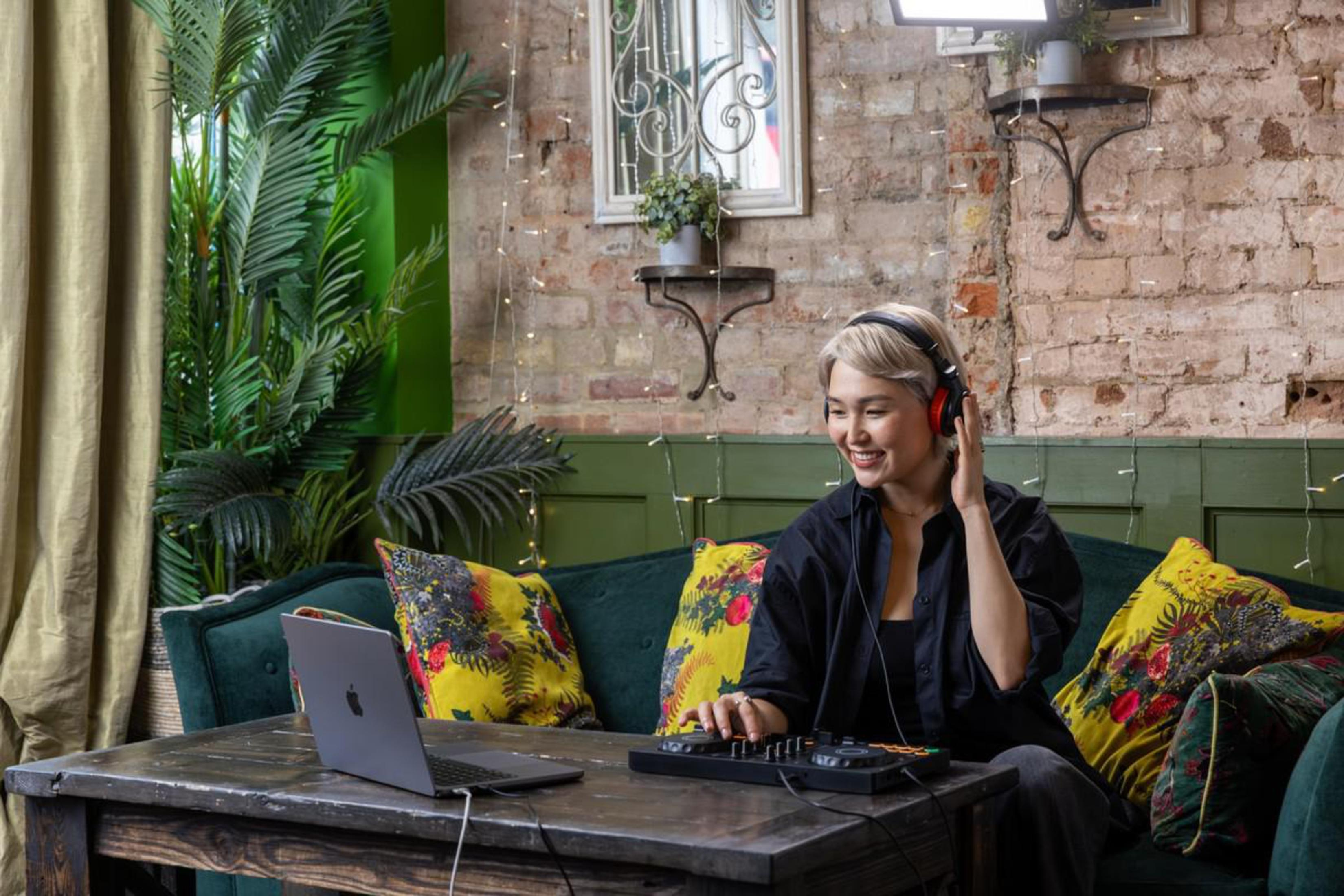 Frau mit Kopfhörern benutzt Laptop und DJ-Mixer im Café.