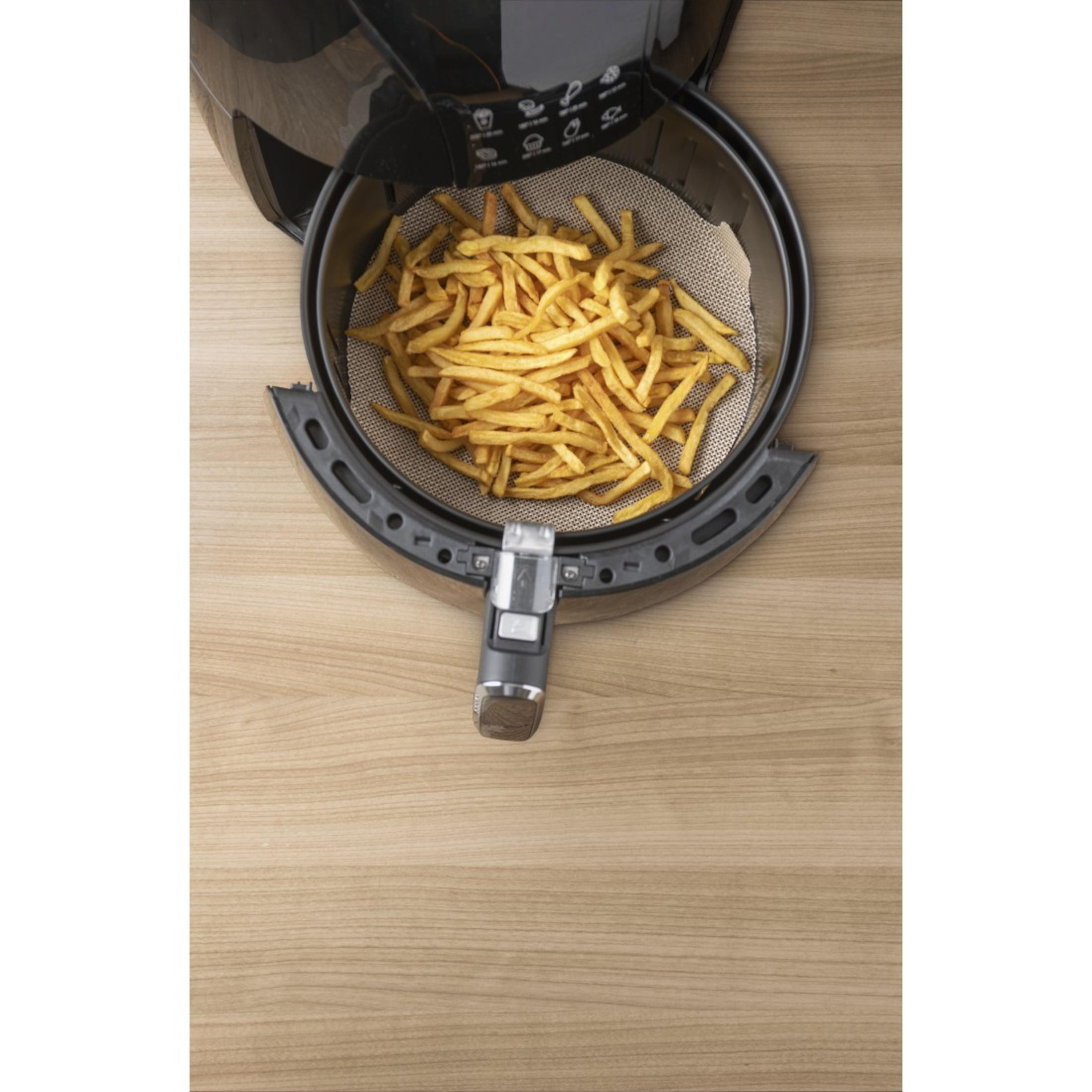Heißluftfritteuse mit Pommes Frites im Korb. Es steht auf einem Holztisch, Draufsicht.