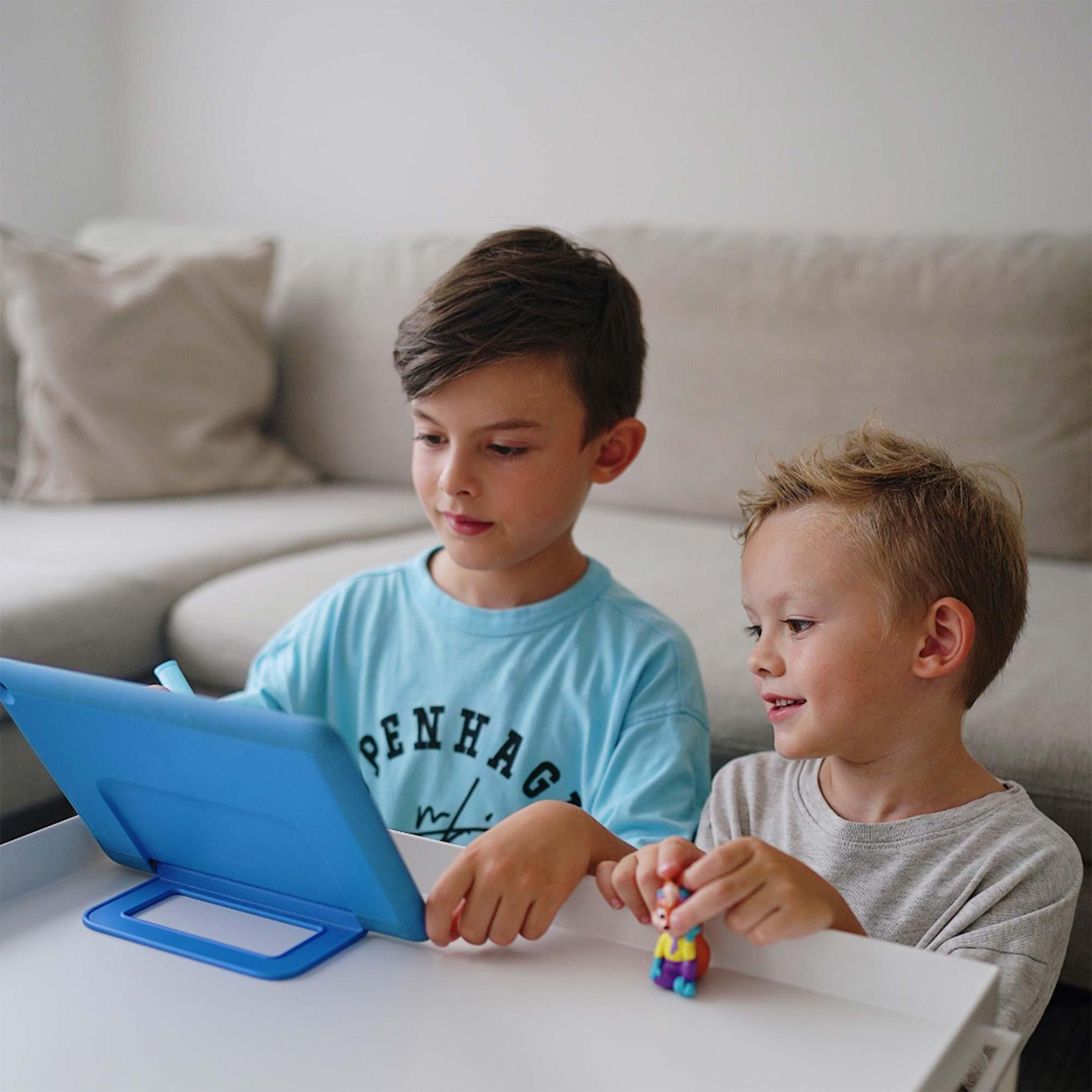 Zwei Jungen sitzen und schauen auf ein blaues Tablet. Einer hält ein Spielzeug. Im Hintergrund ist ein Sofa.