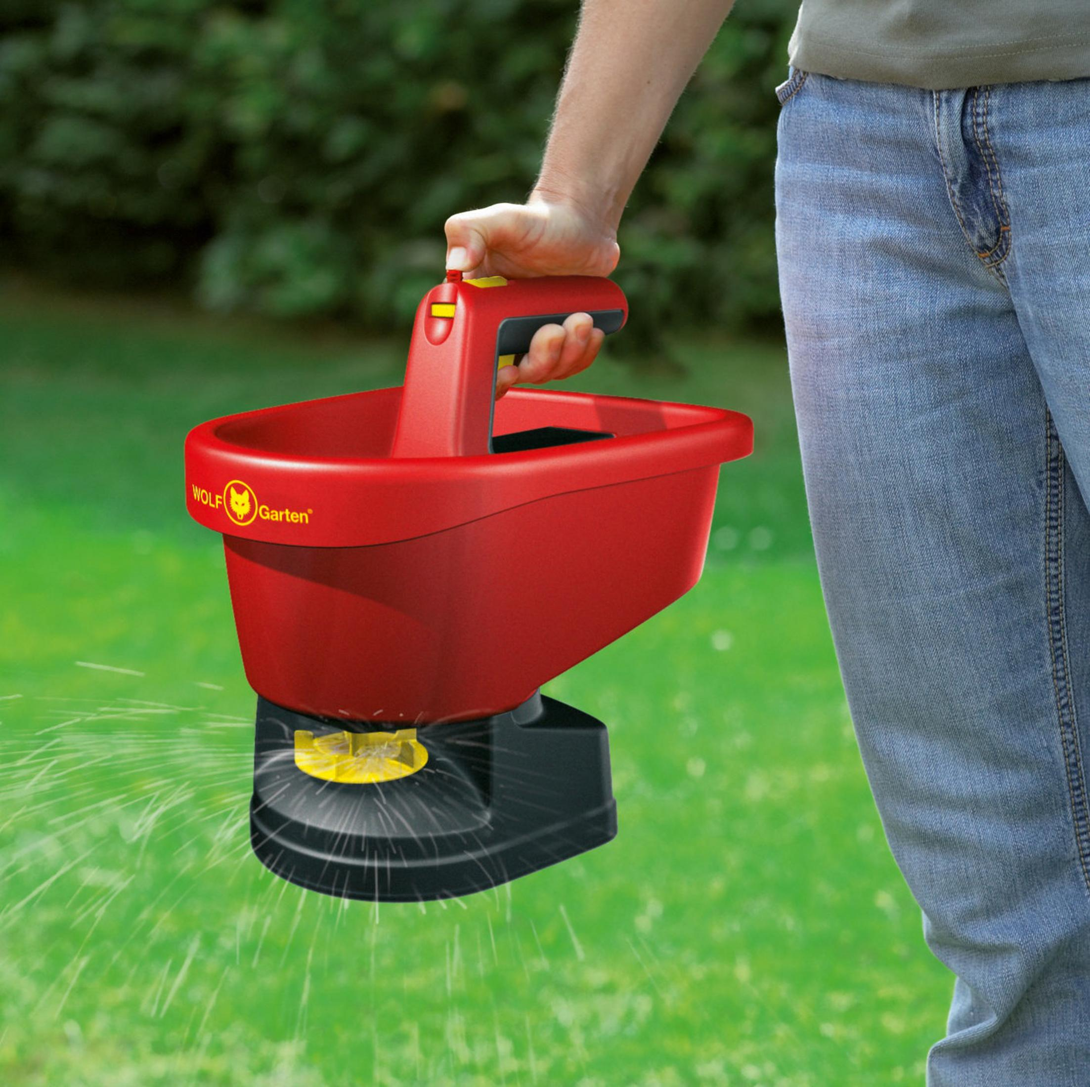 Eine Person hält einen rot-schwarzen Gartenspreizer über grünem Gras.