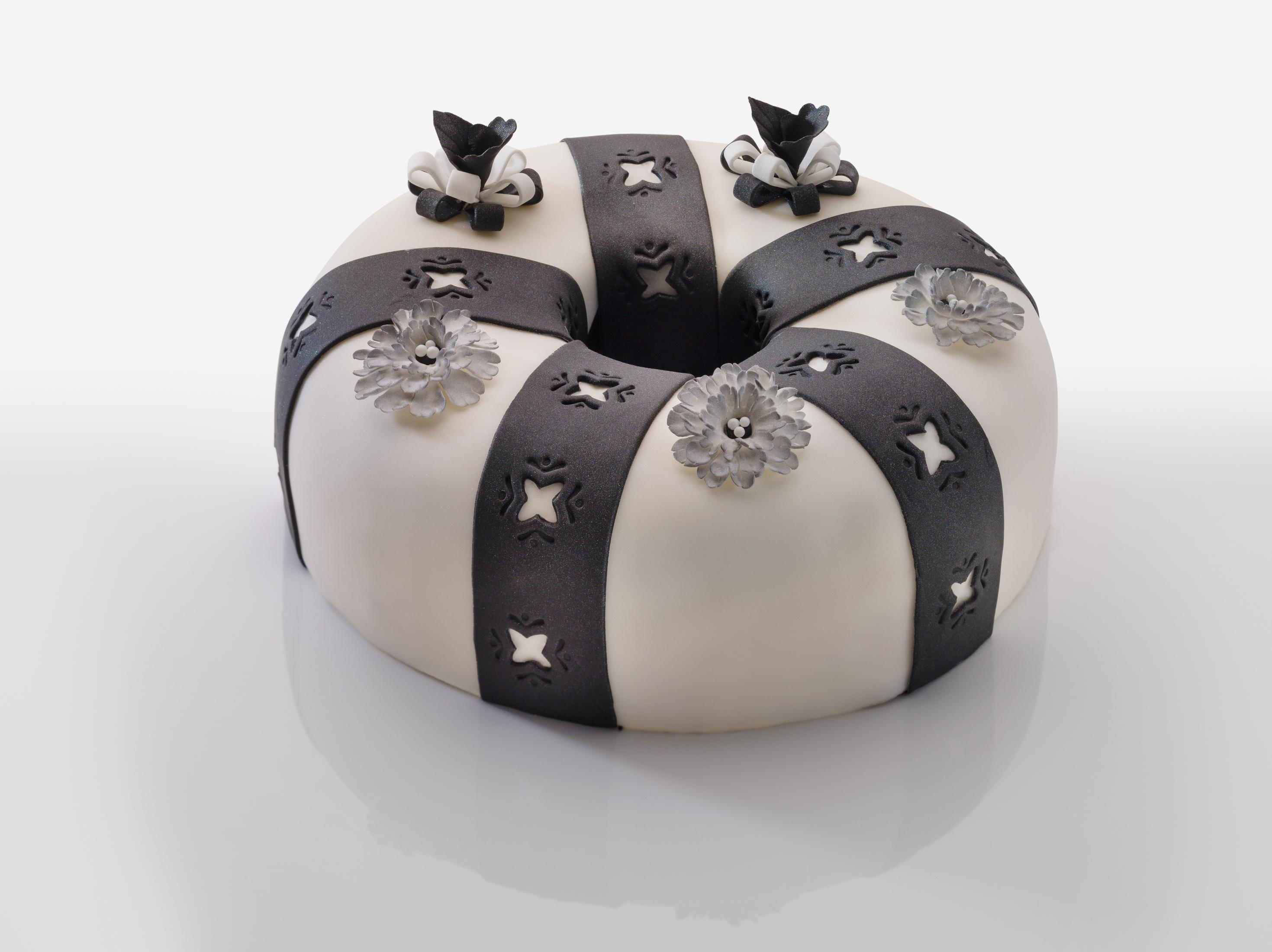 Ein weißer Kuchen in Ringform, verziert mit schwarzen Bändern und Blumen.