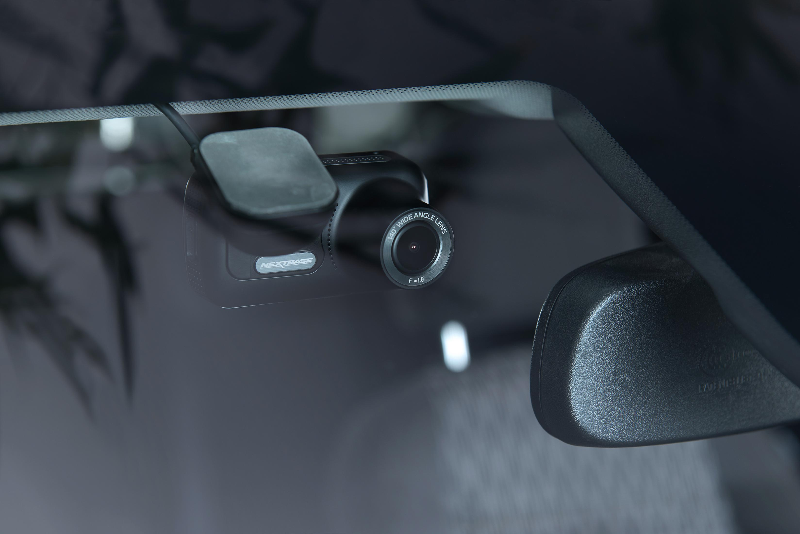 Eine Dashcam, die an einer Windschutzscheibe befestigt ist. Die Kamera ist schwarz. Der Hintergrund ist der Innenraum des Autos.