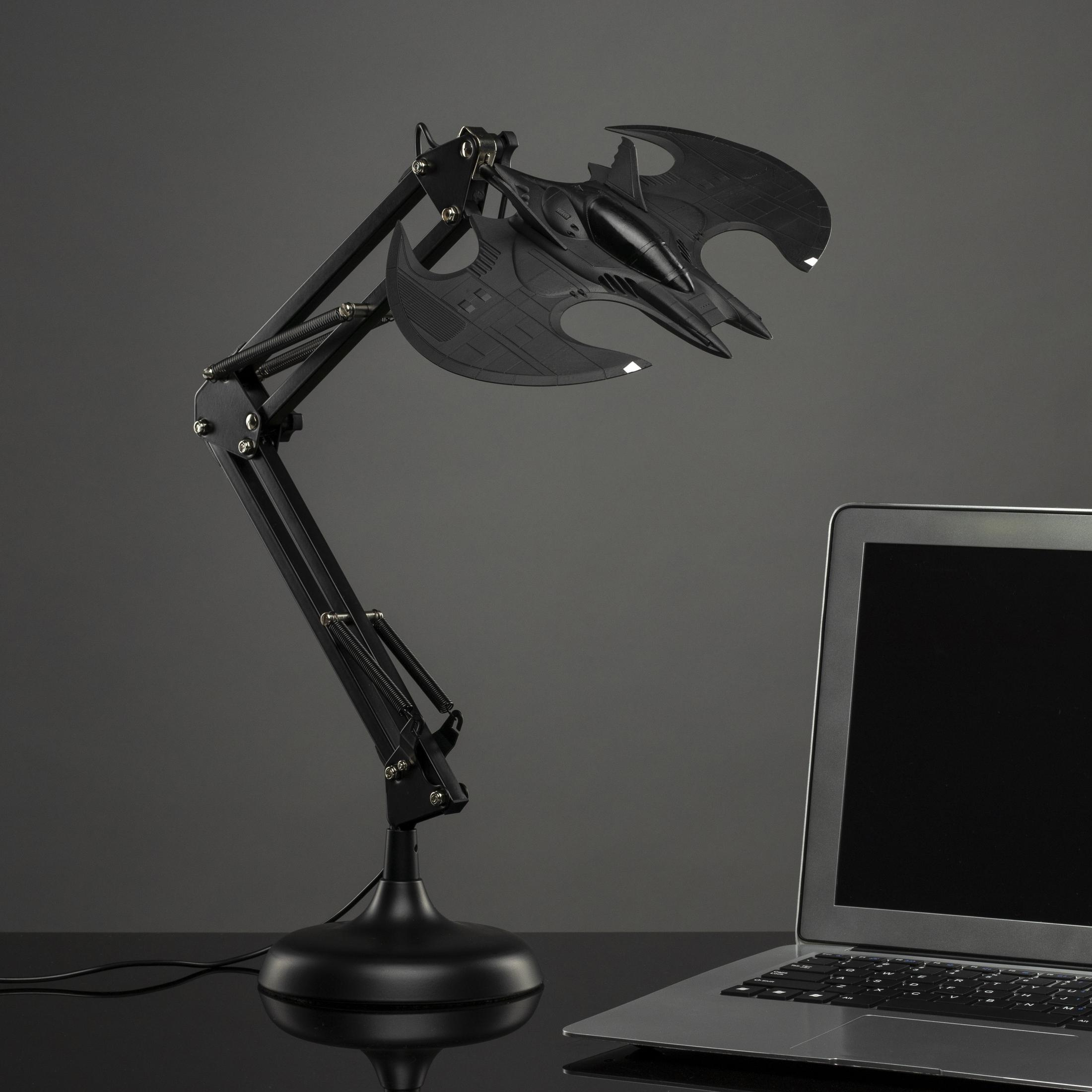Schwarze fledermausförmige Lampe mit einem Laptop auf einer reflektierenden Oberfläche. Die Lampe hat verstellbare Arme.