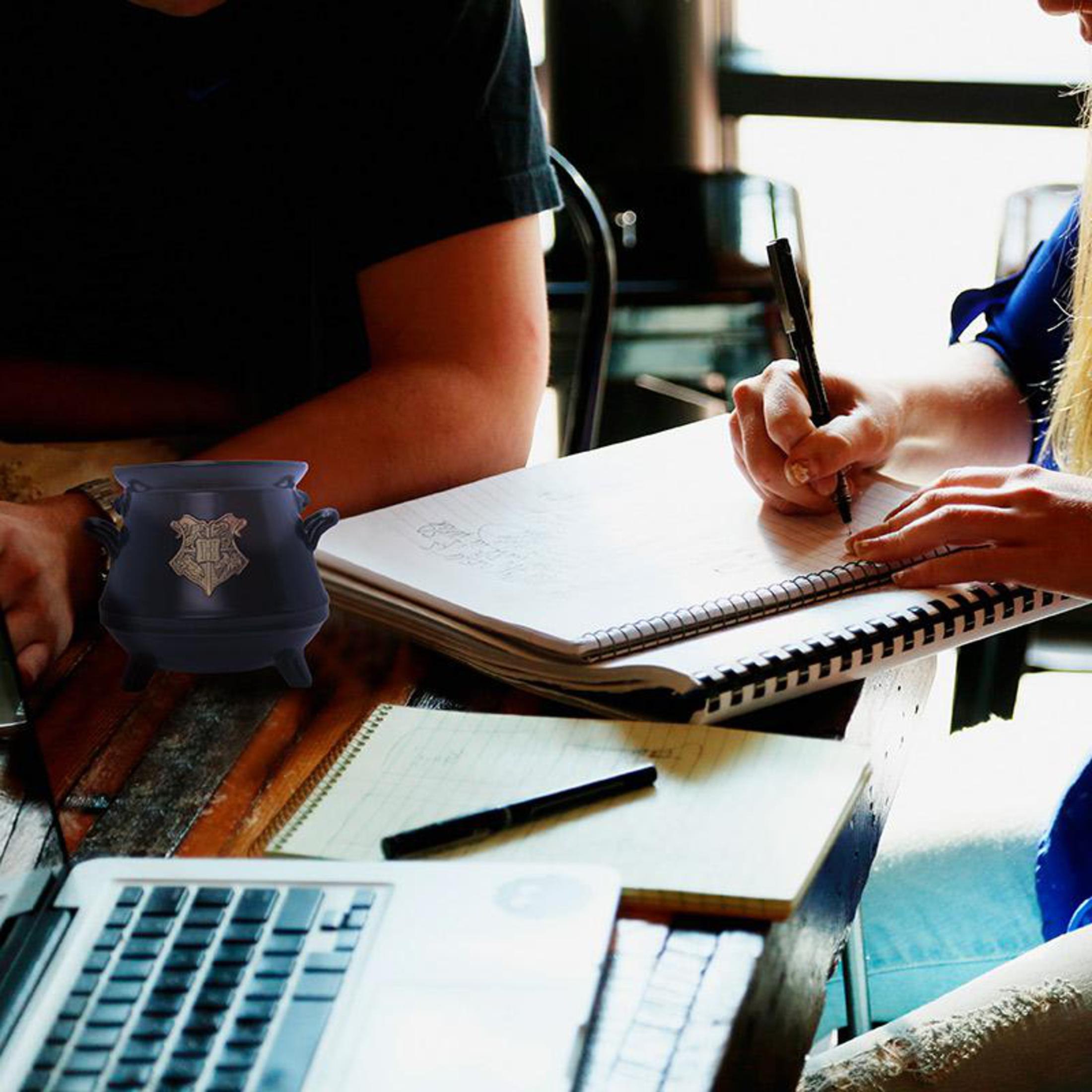 Dwie osoby przy stole, jedna pisze w notatniku, z czarnym kotłem.