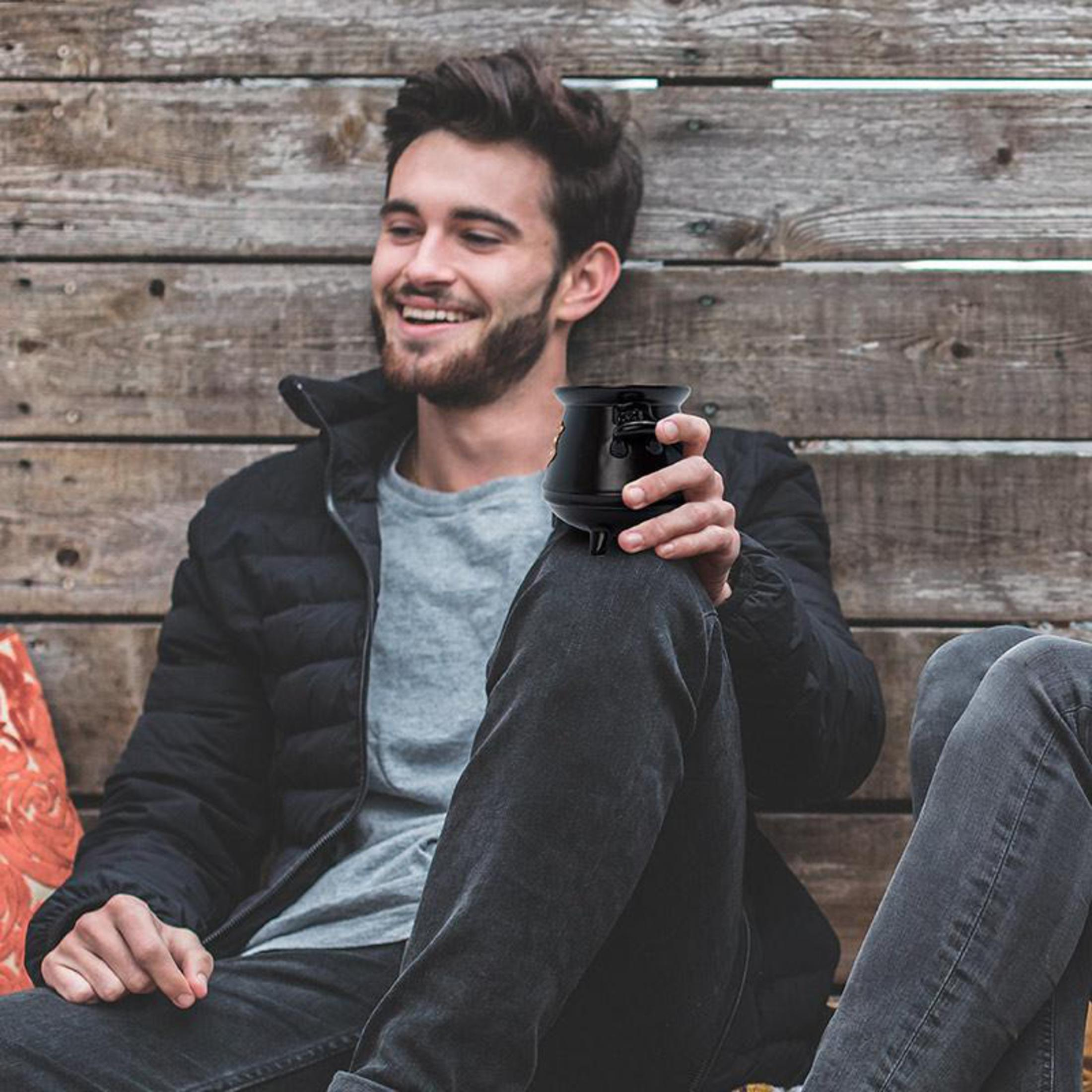 Mężczyzna siedzi trzymając czarny kubek. Uśmiecha się, a w tle jest drewniana ściana.
