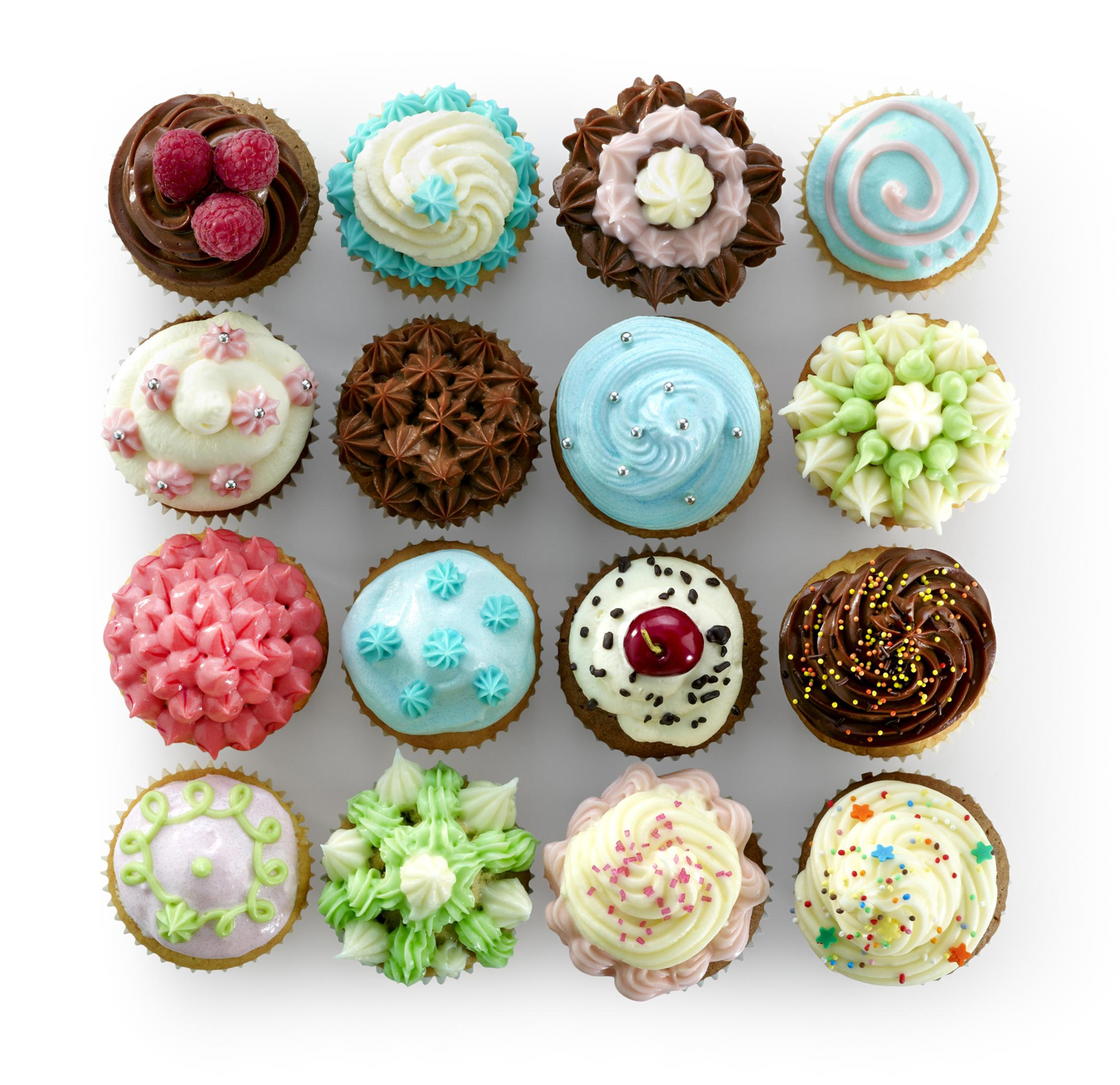 Draufsicht von 16 bunten Cupcakes mit verschiedenen Frostings und Dekorationen auf weißer Oberfläche.