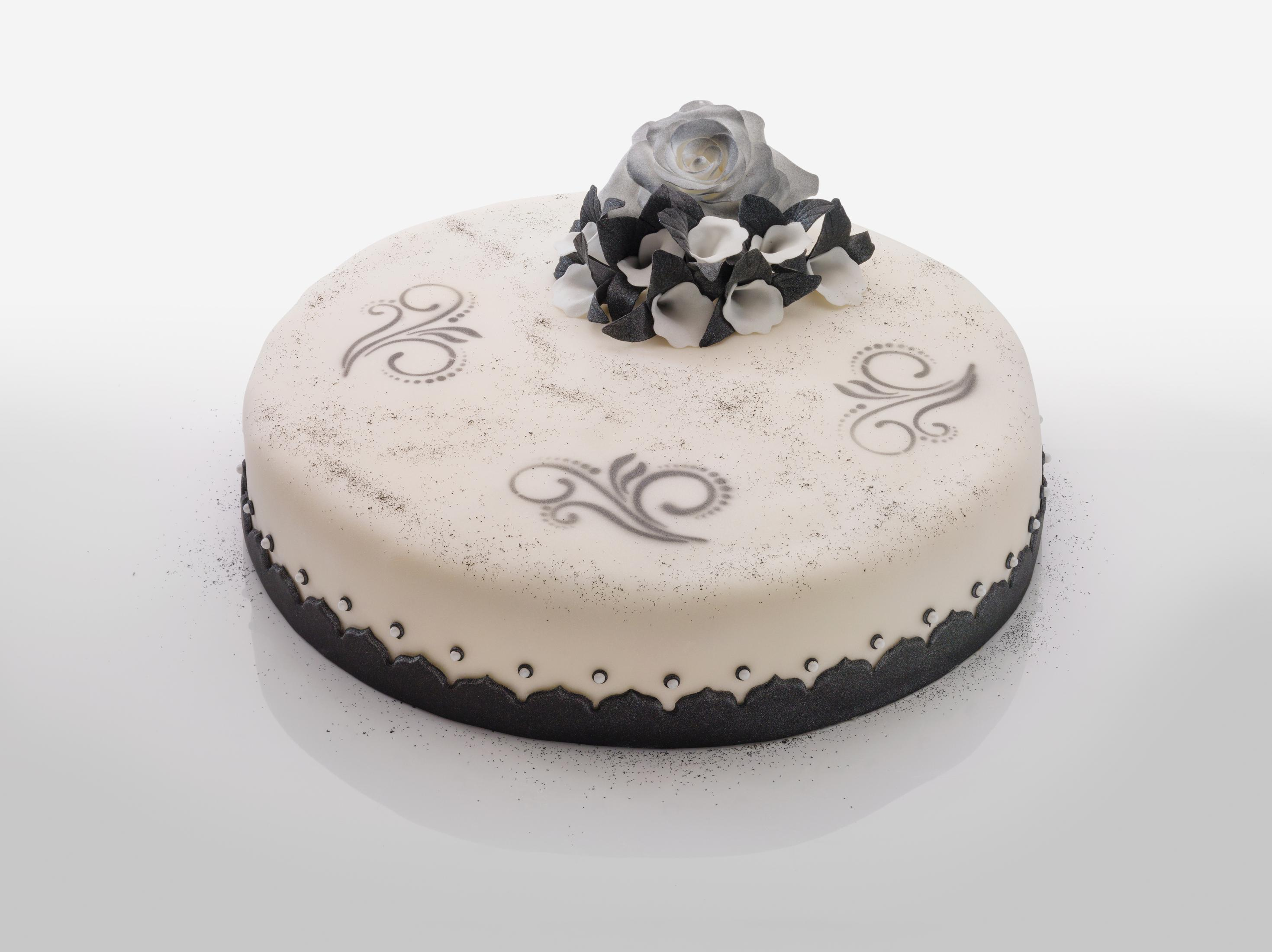 Ein runder, weißer Kuchen mit schwarzem Zuckerguss, Wirbeln und einer grauen Rosen- und Blumendekoration.