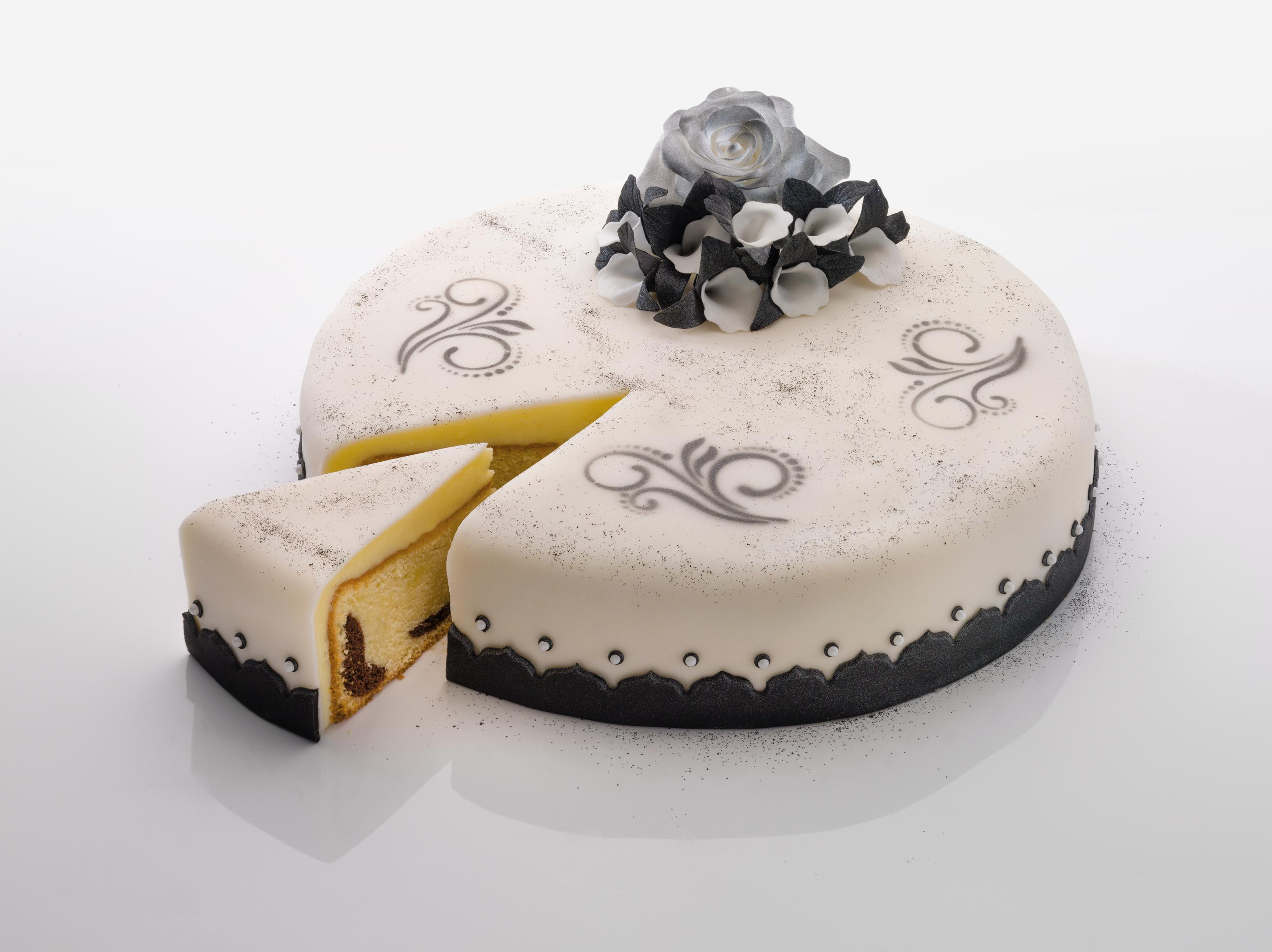 Ein Kuchen mit einem entfernten Stück, verziert mit weißem Zuckerguss, schwarzen Wirbeln und einer Blume oben.