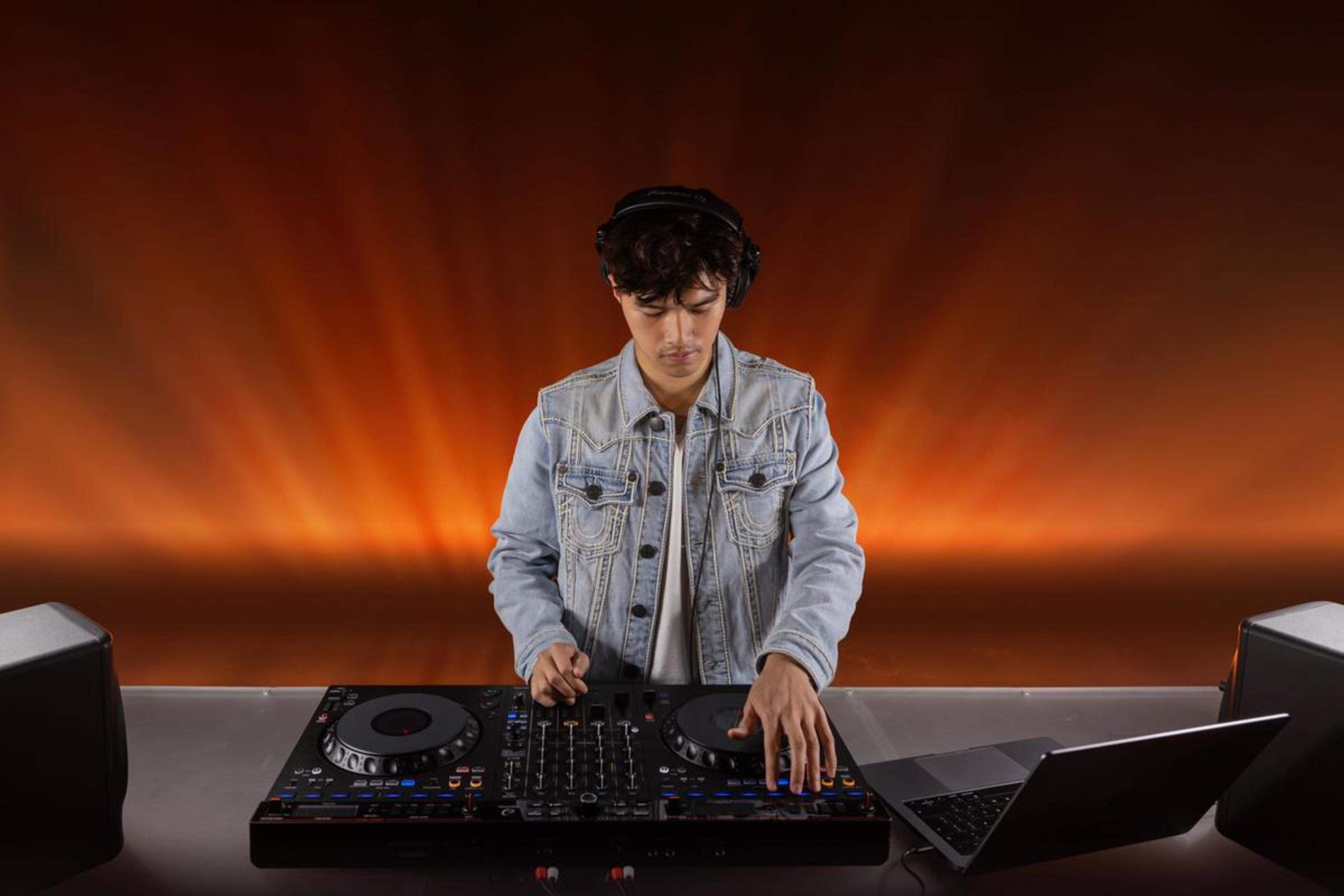 DJ in giacca di jeans che utilizza un controller DJ con un laptop.