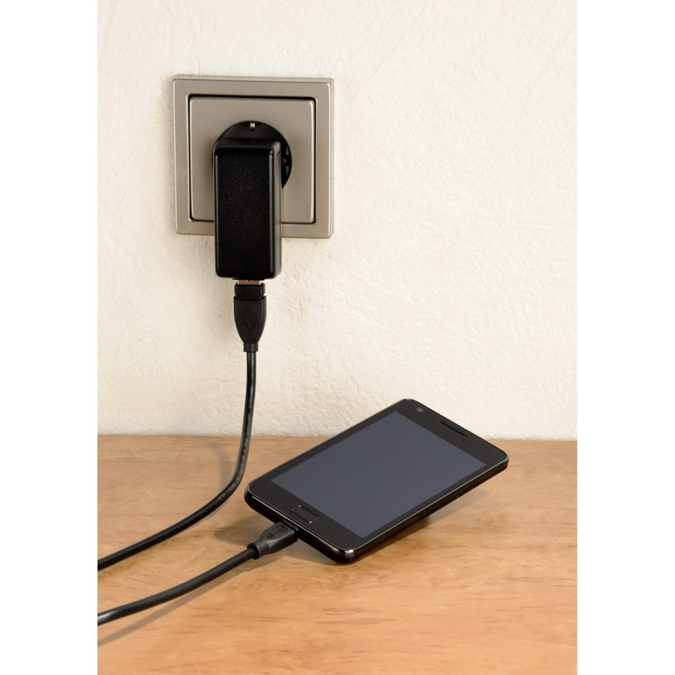 Ein Smartphone wird auf einem Holztisch geladen, angeschlossen an eine Steckdose.