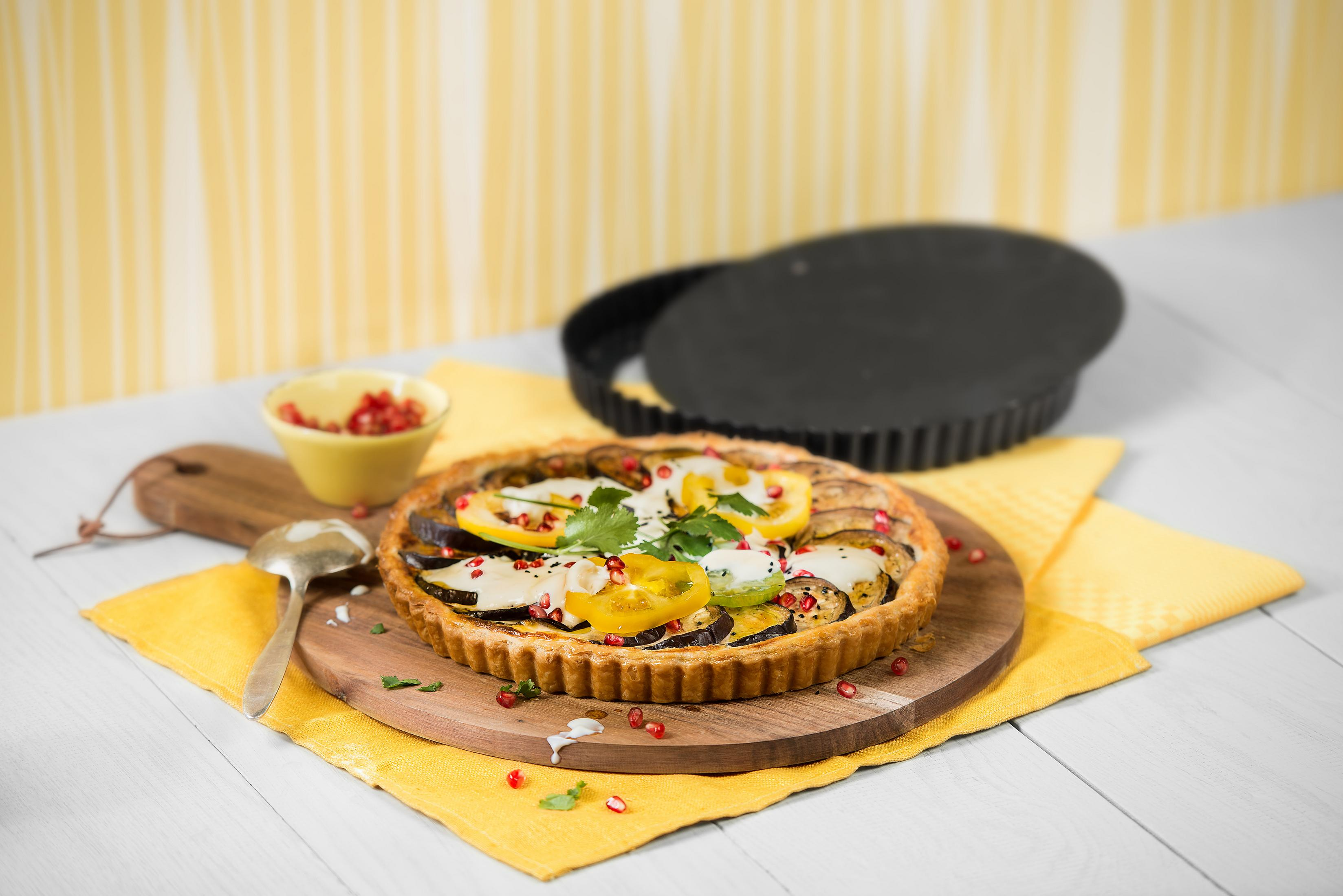 Ein Tart mit Gemüse, ein Holzbrett und ein gelber Hintergrund.