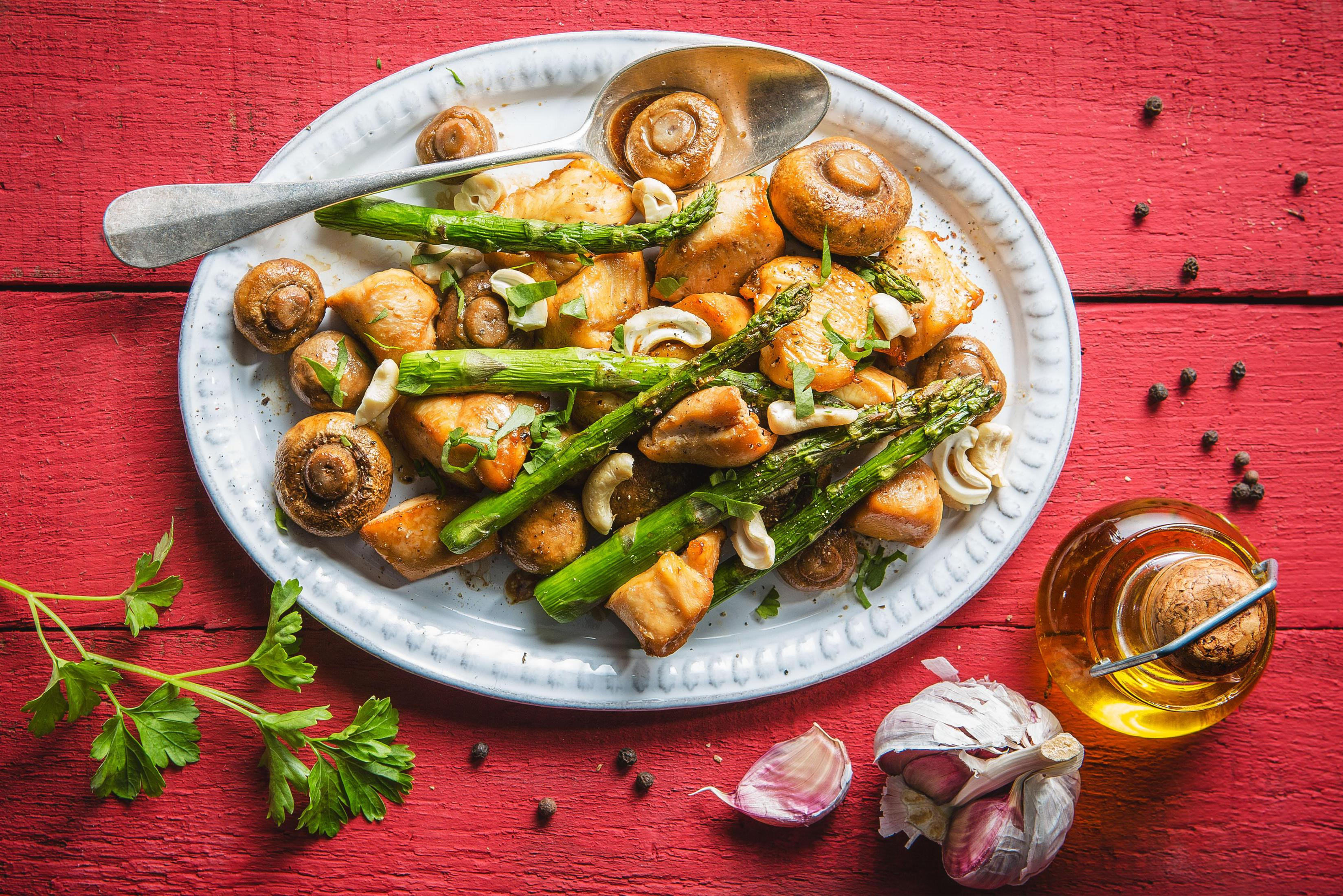 Plate of food with chicken, asparagus, mushrooms, cashew nuts, and oil.