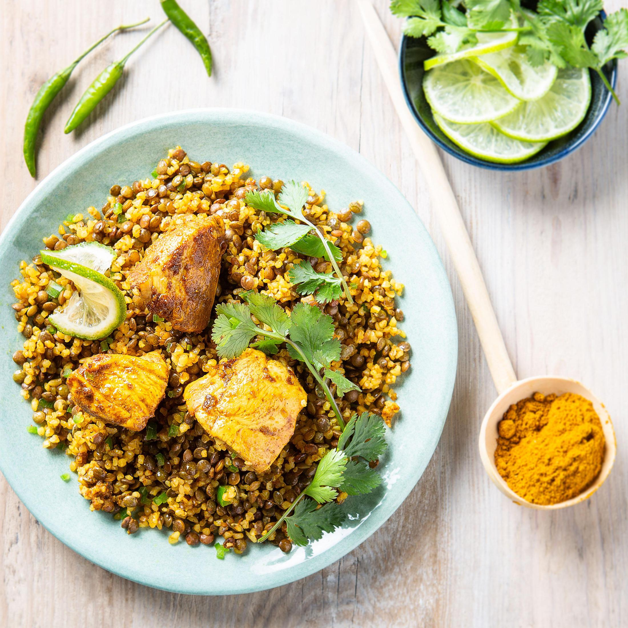 A plate of food with chicken and lentils, garnished with cilantro, limes, and chili peppers.