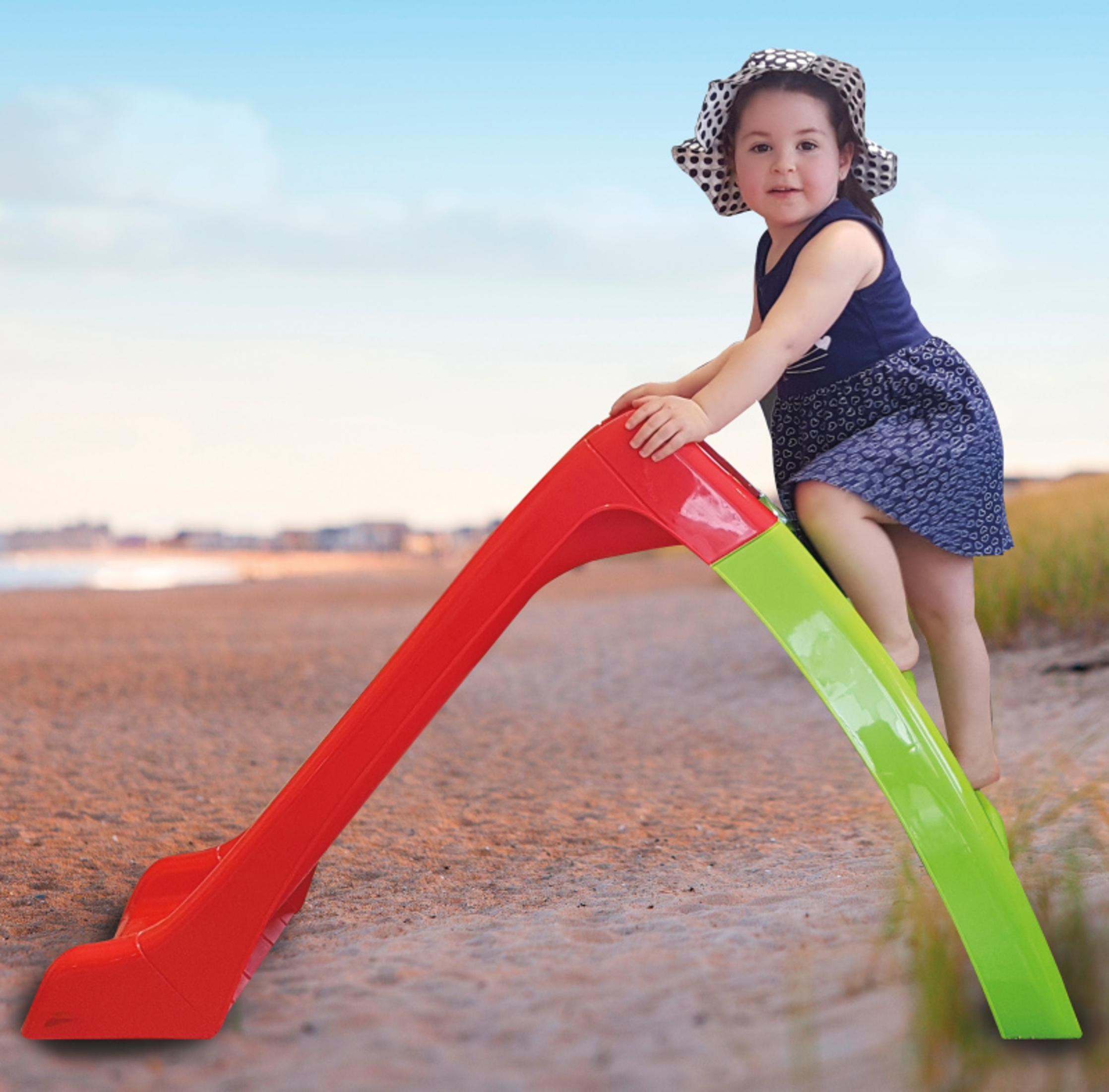 Ein Mädchen auf einer rot-grünen Rutsche am Strand.