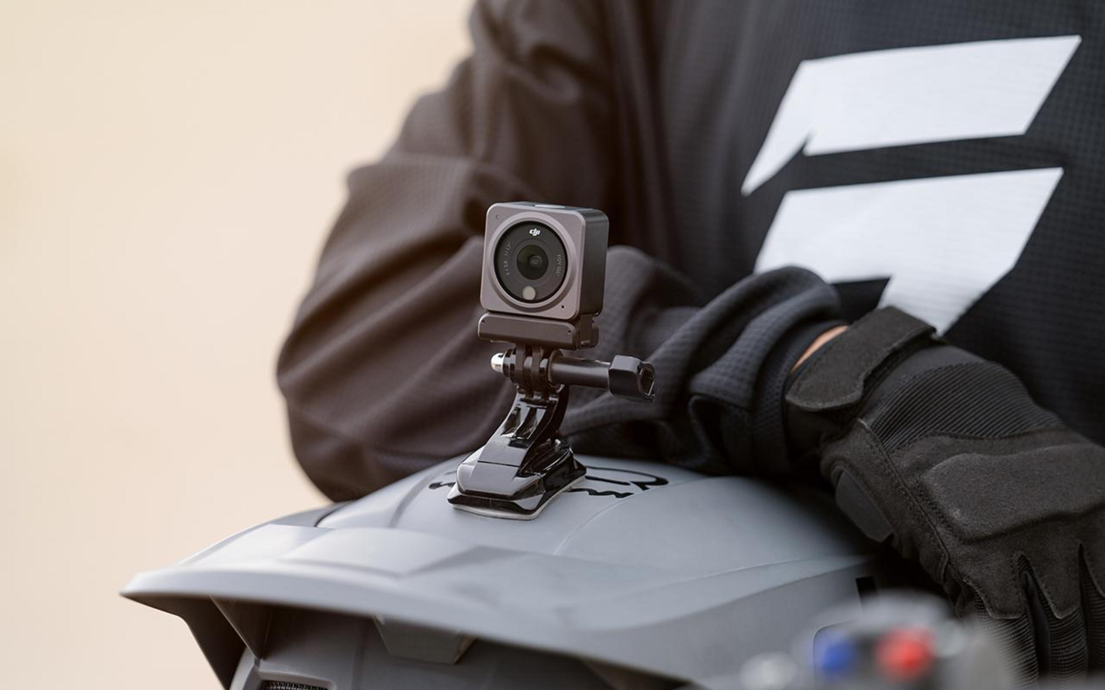 Kamera sportowa na kasku, trzymana przez osobę w czarnych rękawicach.