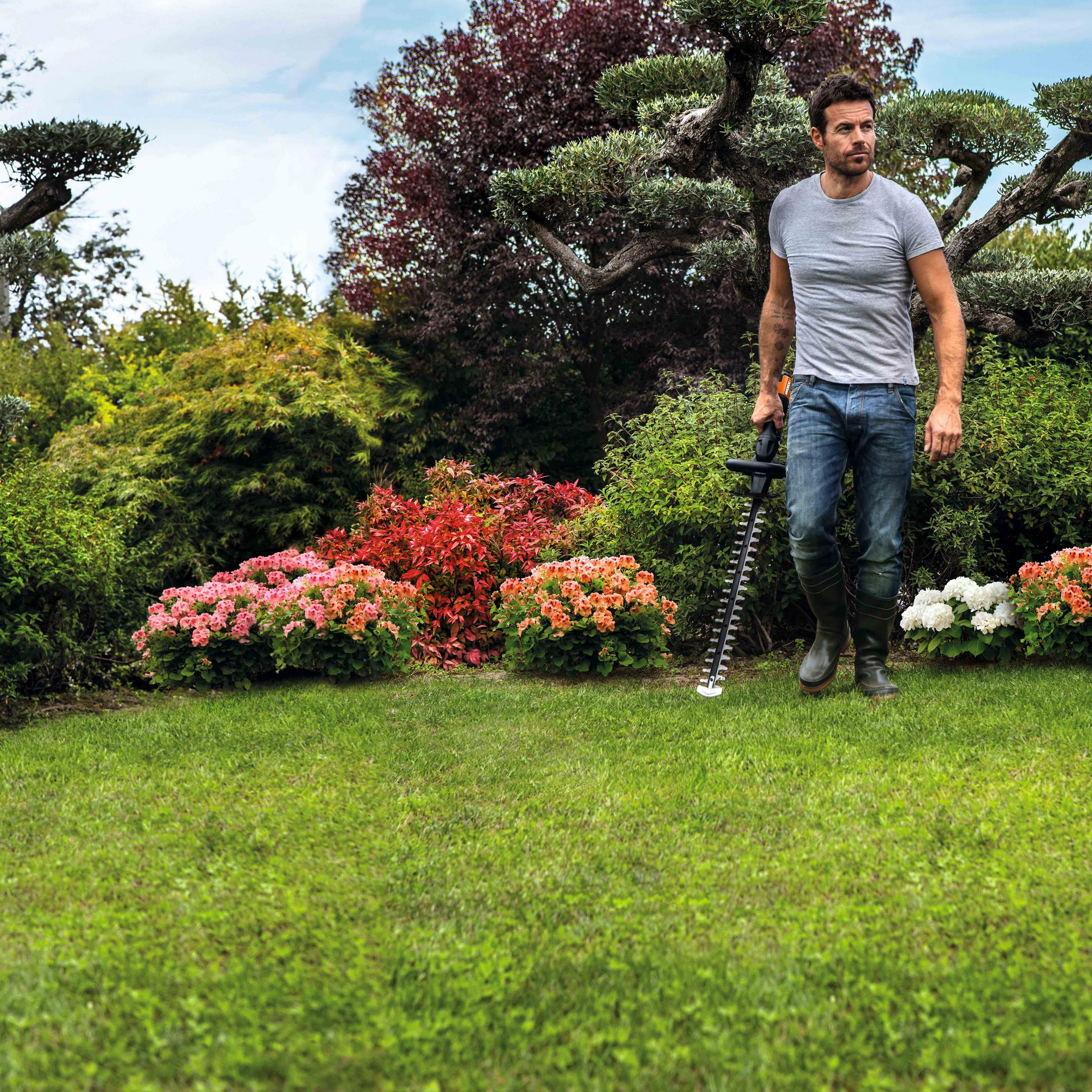 Ein Mann benutzt eine Heckenschere in einem Garten. Im Hintergrund sind Blumen und Bäume.