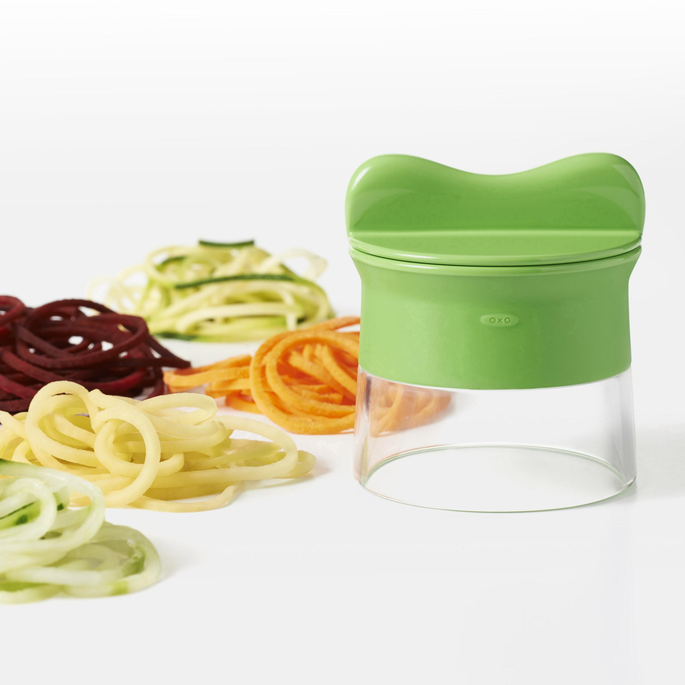 Ein grüner Spiralschneider mit verschiedenen Gemüsespiralen auf einer weißen Oberfläche.