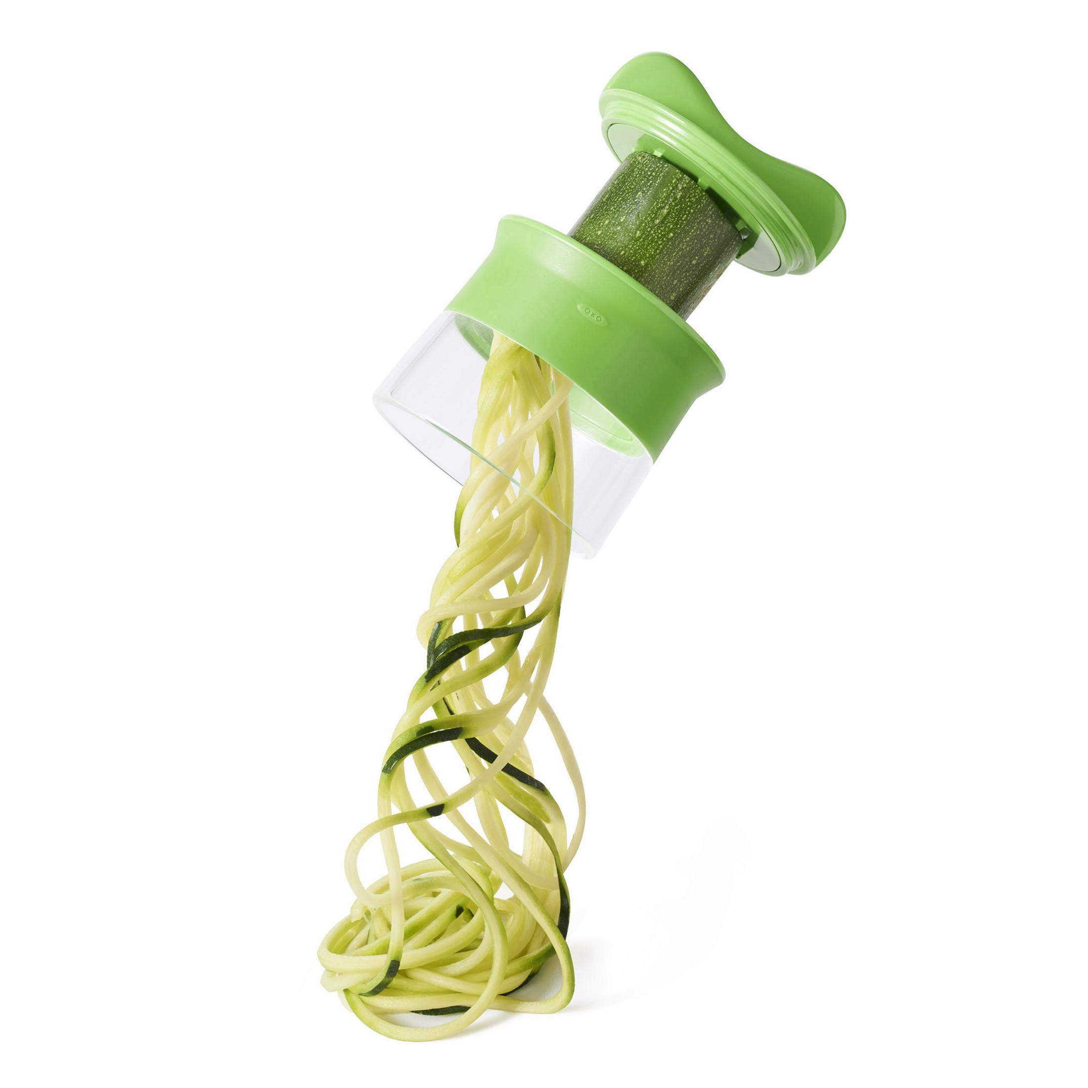 Ein grüner Spiralschneider mit einer Zucchini. Ein Haufen spiralisierter Zucchini fällt darunter.