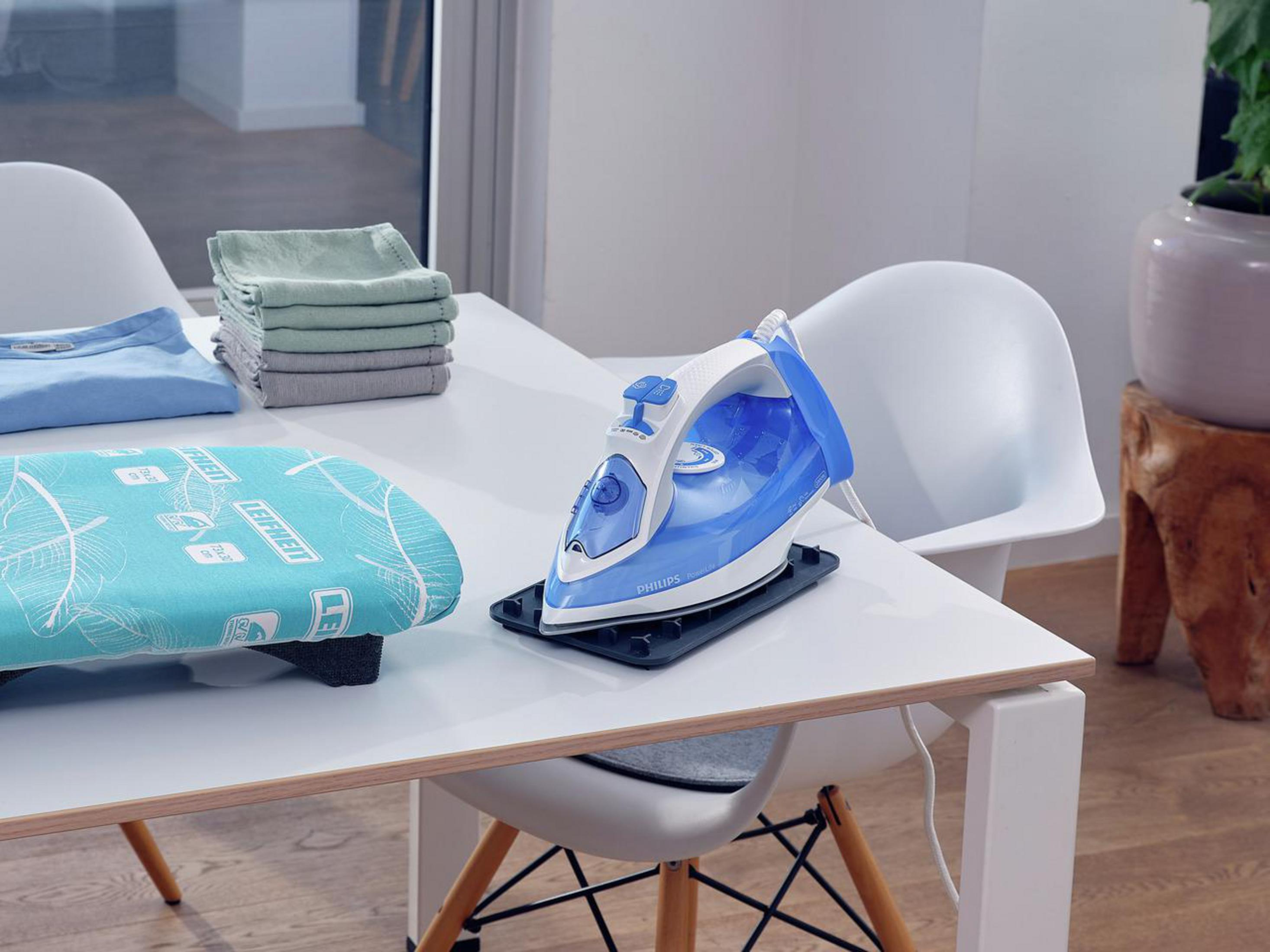 Deska do prasowania z żelazkiem, ubraniami i złożonymi ręcznikami na białym stole.