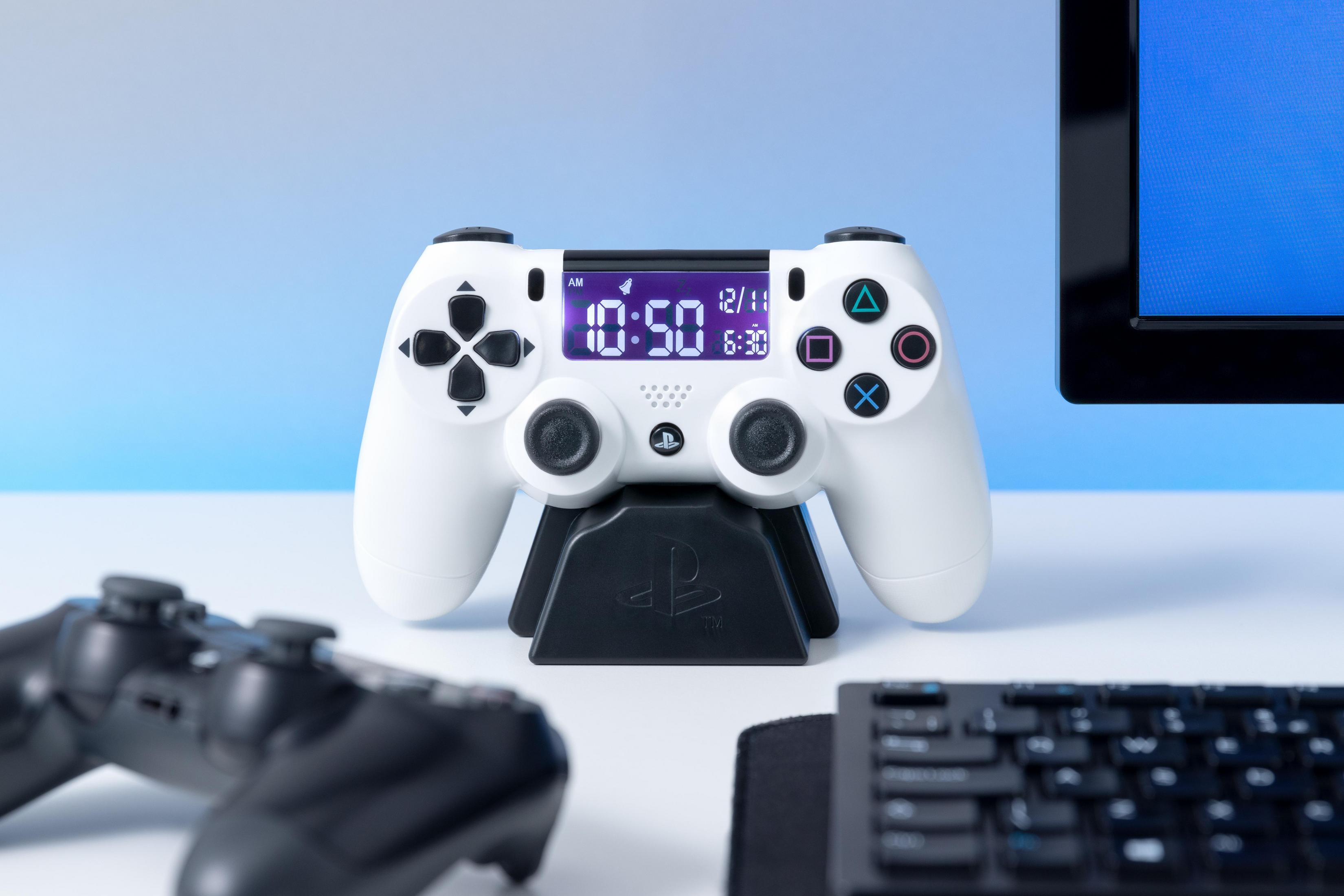 Weißer PS4-Controller auf einem schwarzen Ständer, der Zeit und Datum anzeigt. Ein weiterer Controller und eine Tastatur sind da.