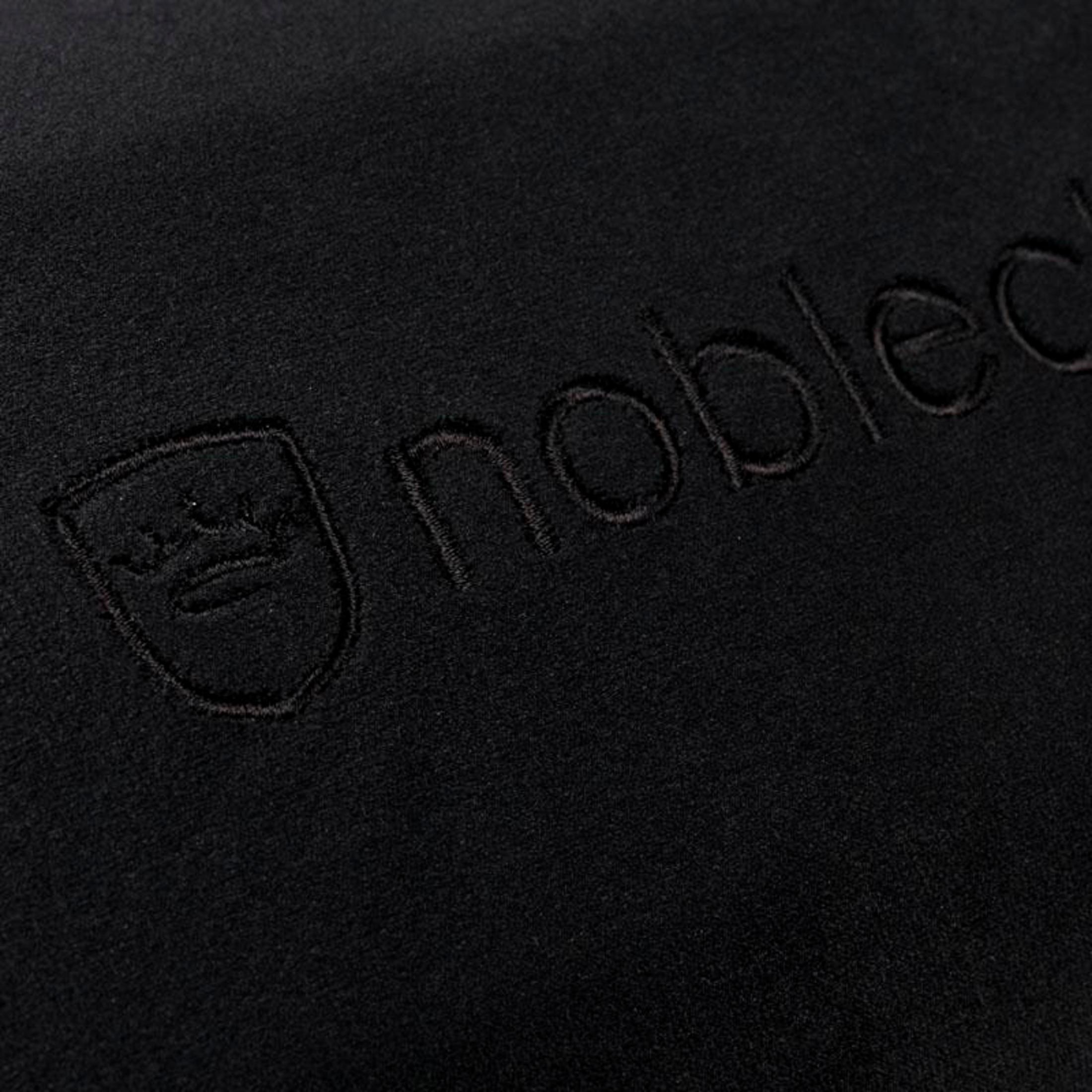 Nahaufnahme eines schwarzen Stoffes mit gesticktem "noble" Text und einem Kronenlogo.